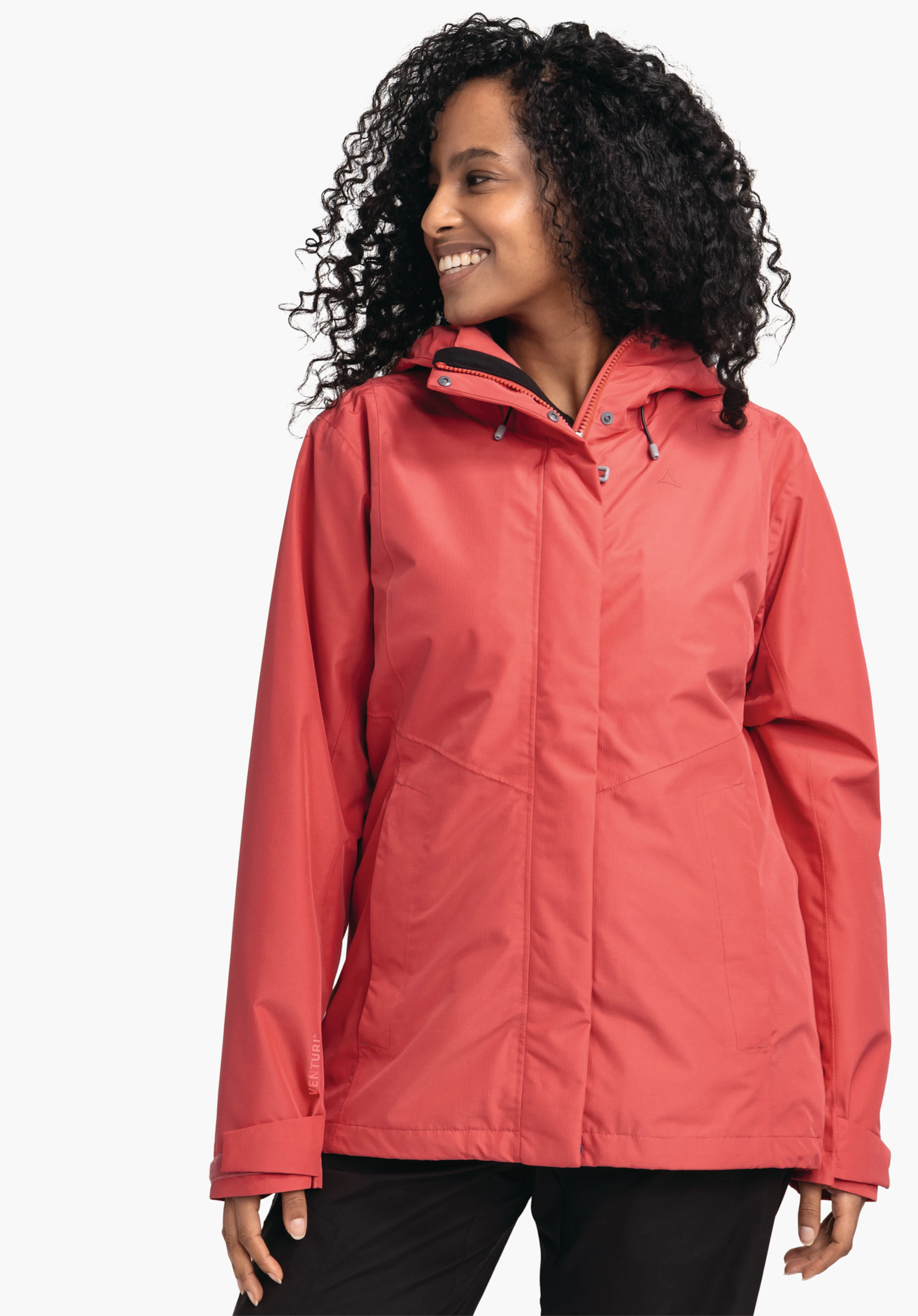 3in1 Jacket Style Okere WMS Rote Jacke, getragen von Frau mit lockigem Haar; sie lächelt und schaut zur Seite, vor hellem Hintergrund. Schöffel-Logo auf der Brust. Text auf Ärmel: "VENTURI".