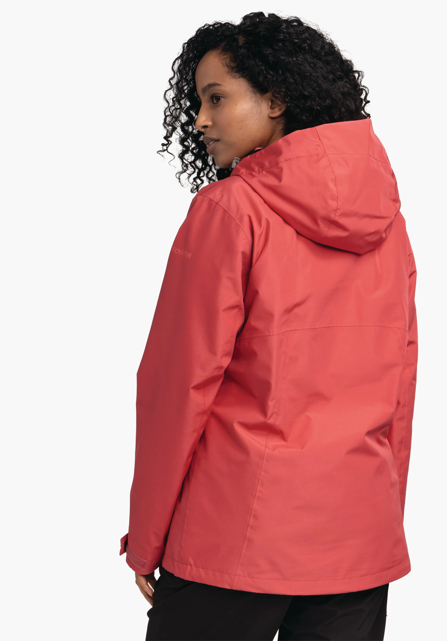 3in1 Jacket Style Okere WMS Rote Jacke, getragen von Person, die sich halb nach links dreht; Kapuze liegt am Rücken; weißer Hintergrund. Text auf Ärmel: Schöffel.