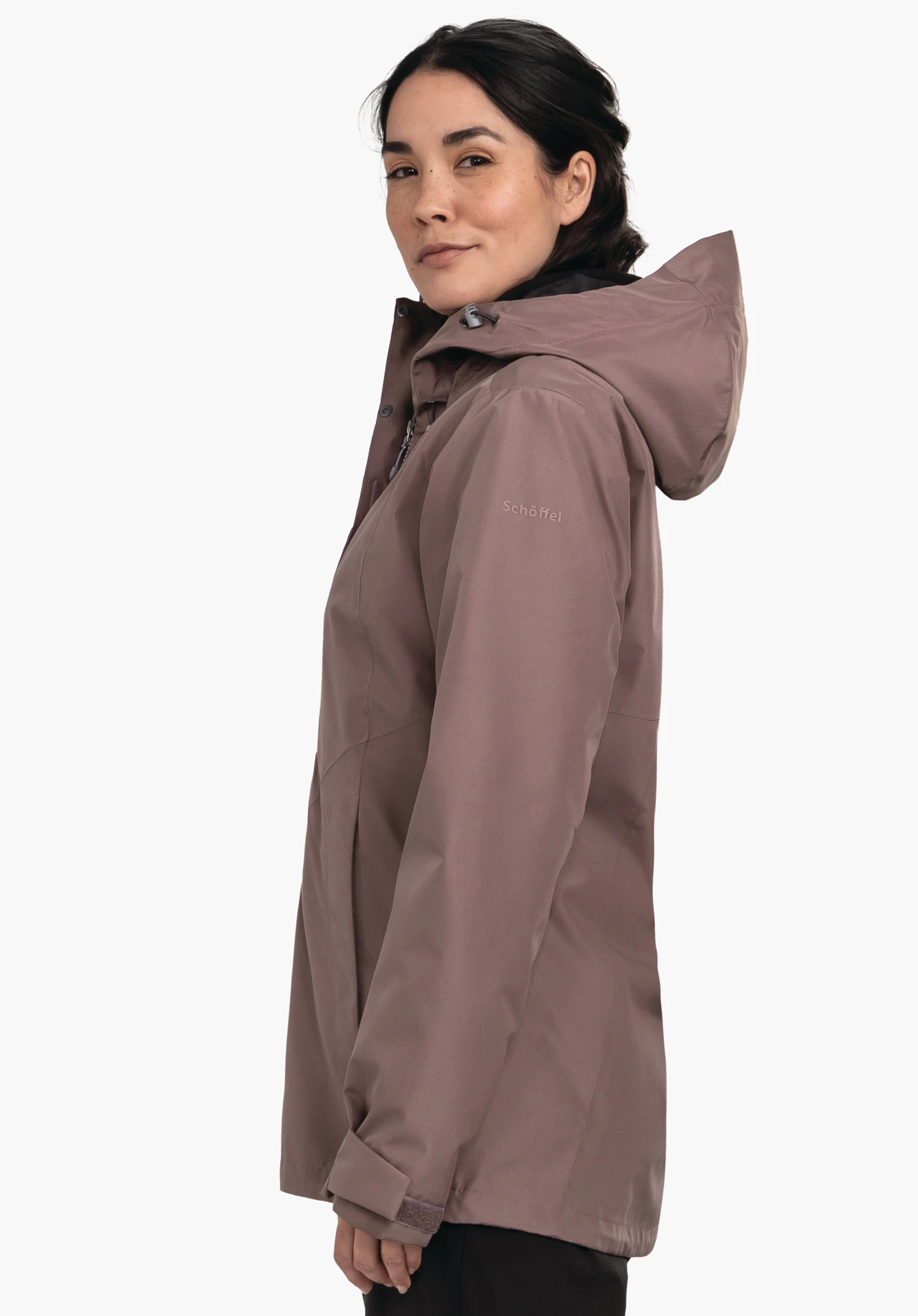 3in1 Jacket Style Okere WMS veste imperméable violet foncé avec capuche, portée de profil par une femme; elle regarde légèrement vers la caméra, fond blanc. Texte sur la manche: "Schöffel".