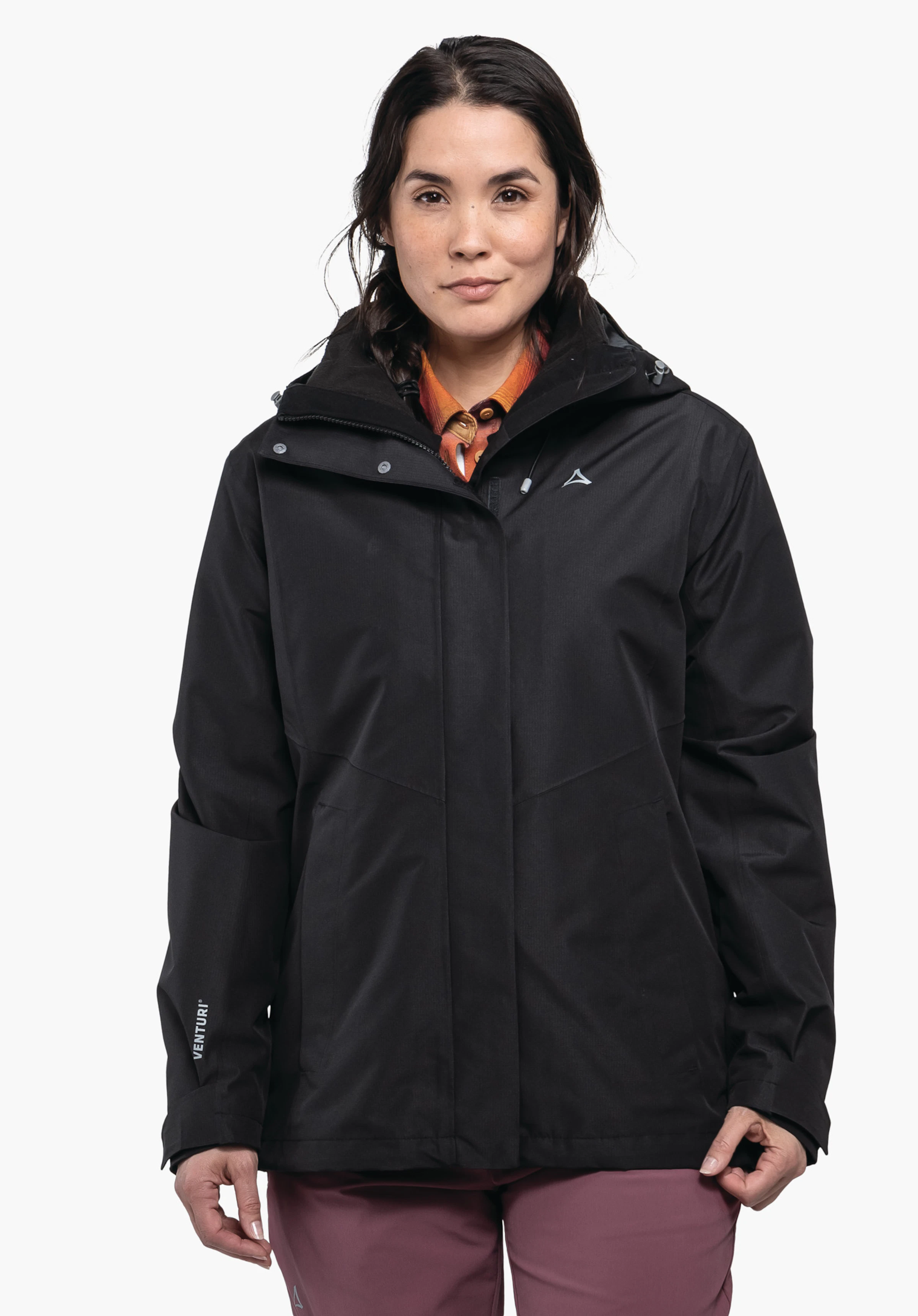 3in1 Jacket Style Okere WMS zwarte jas, gedragen door een frontaal staande persoon voor witte achtergrond; Schöffel-logo op de borst, opschrift "VENTURI" op de linker mouw; oranje overhemdkraag zichtbaar, roze broek.