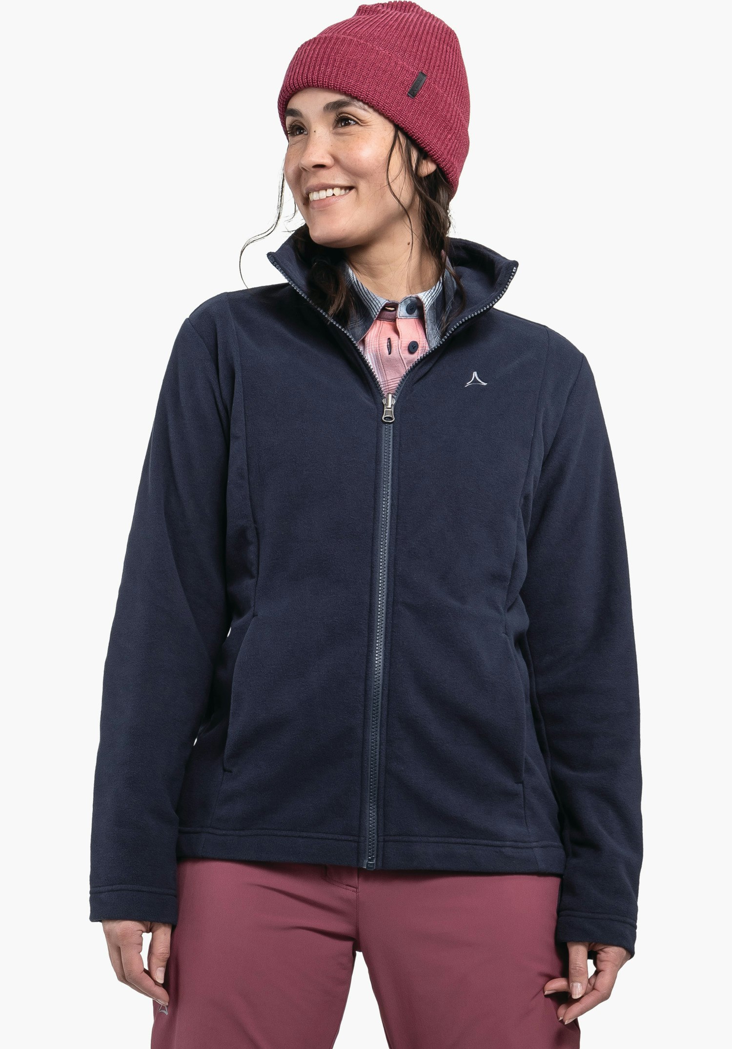 3in1 Jacket Style Okere WMS veste polaire bleu foncé; femme souriante regardant vers la droite; elle porte un bonnet rouge foncé et un pantalon rouge clair; logo Schöffel sur la poitrine; fond blanc.