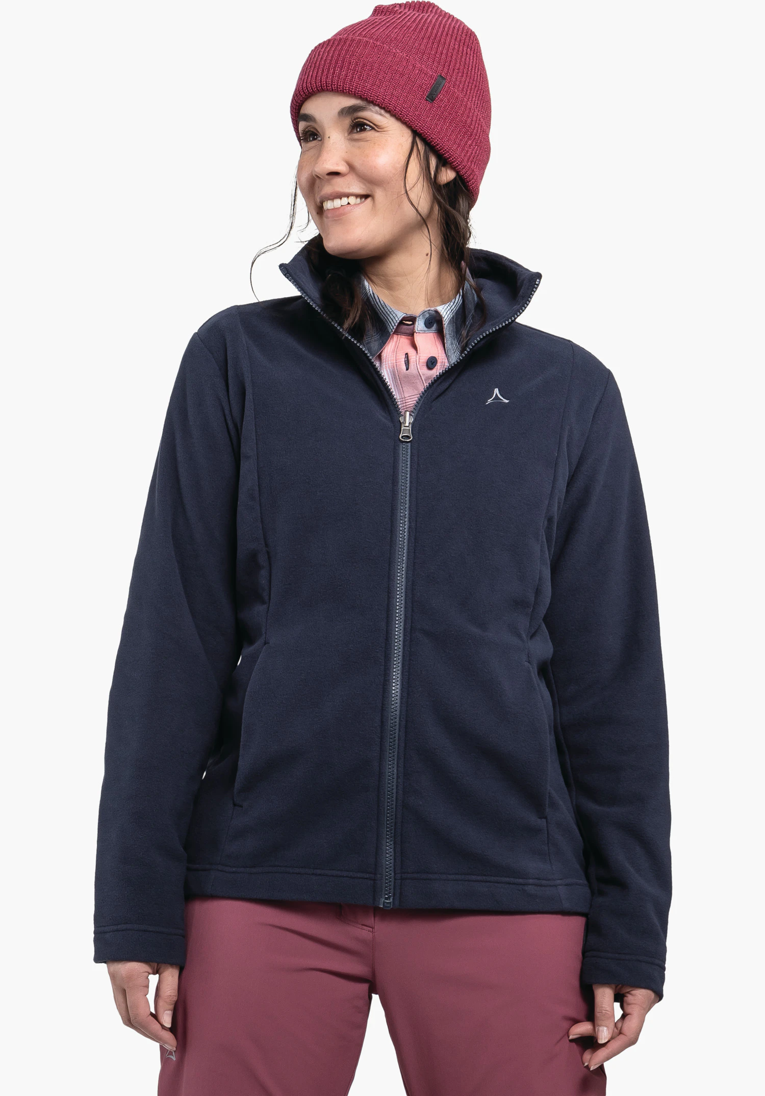 3in1 Jacket Style Okere WMS dunkel blaue Fleecejacke; Frau lächelt und schaut nach rechts; sie trägt dunkel rot Mütze und hell rot Hose; Schöffel-Logo auf Brust; weißer Hintergrund.