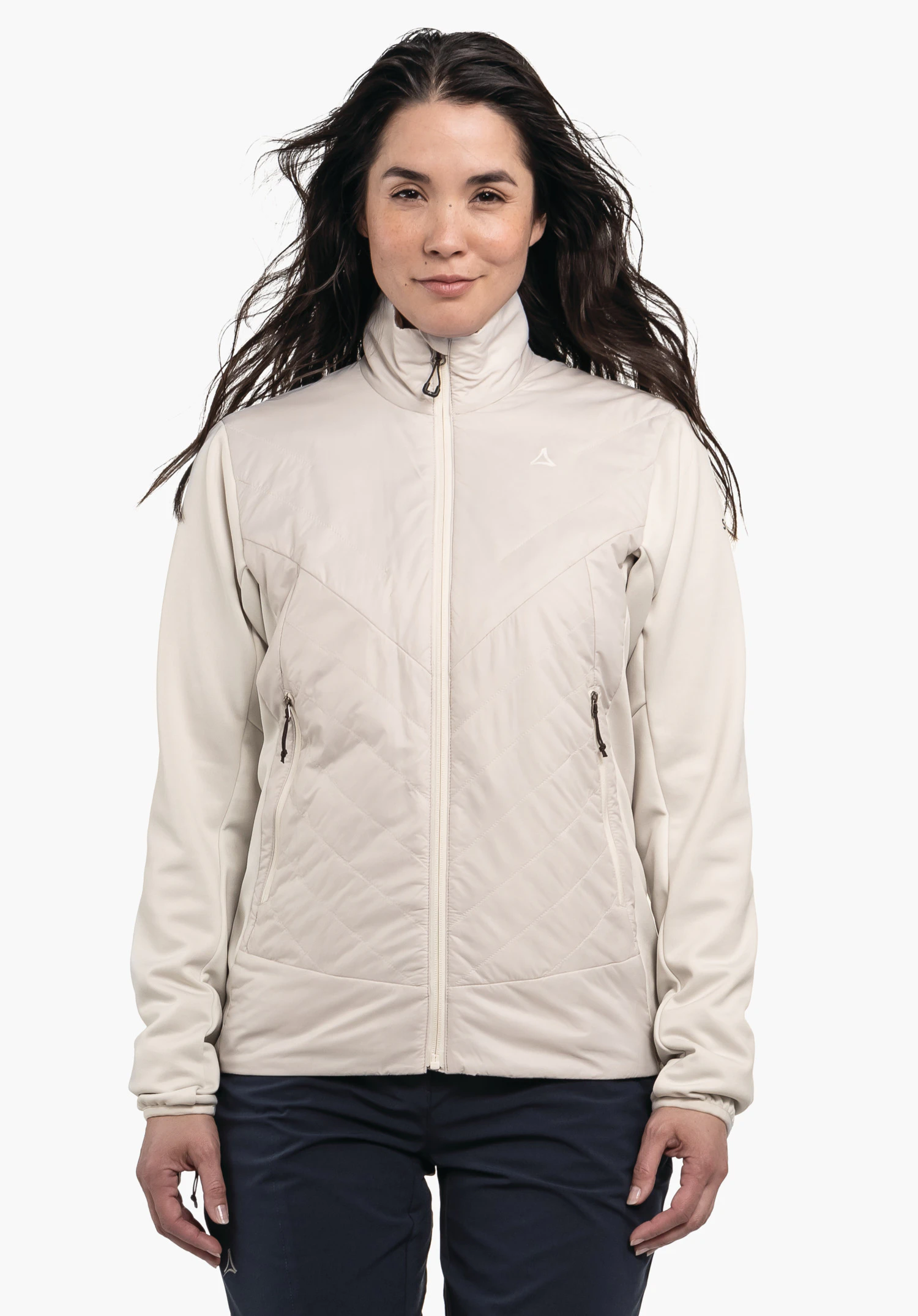 Hybrid Jk Style Cascata WMS Veste beige clair zippée à l’avant avec poches zippées et logo Schöffel sur la poitrine; portée par une femme debout aux cheveux légèrement balayés par le vent; fond clair uni.