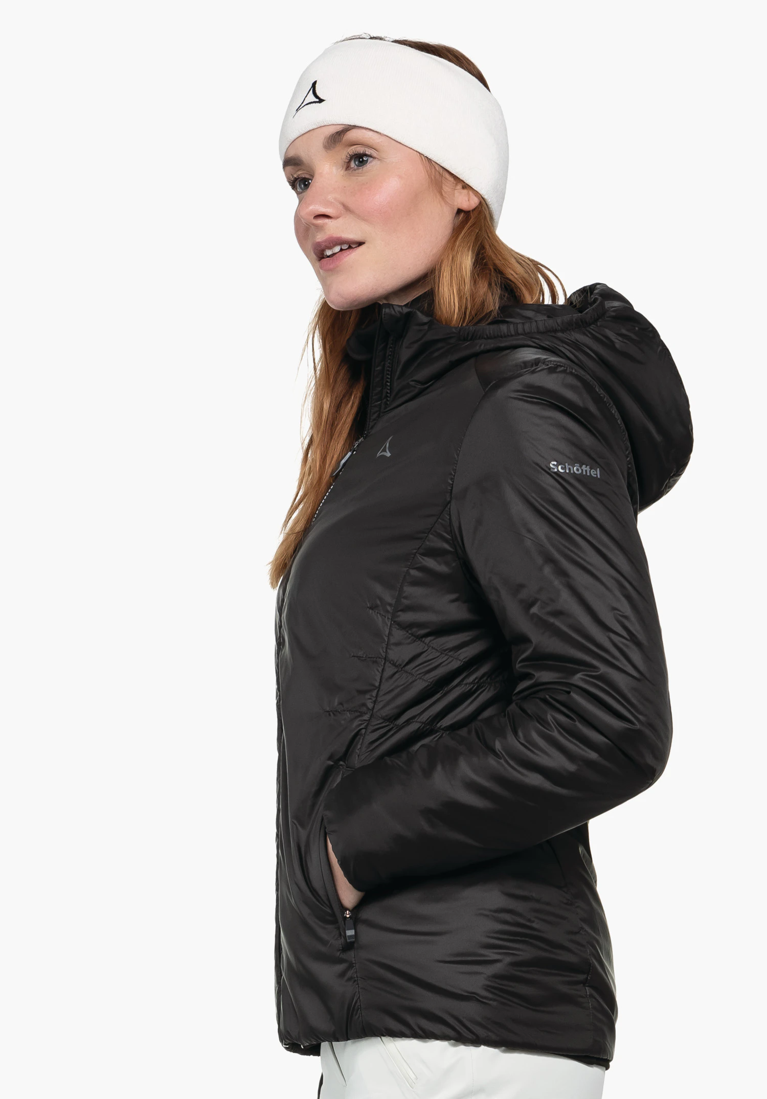 Ins Jacket Style Pontre WMS woman in a black hooded jacket with hands in pockets, looking slightly upwards to the side; wearing a white headband with Schöffel logo; sleeve lettering: "Schöffel".