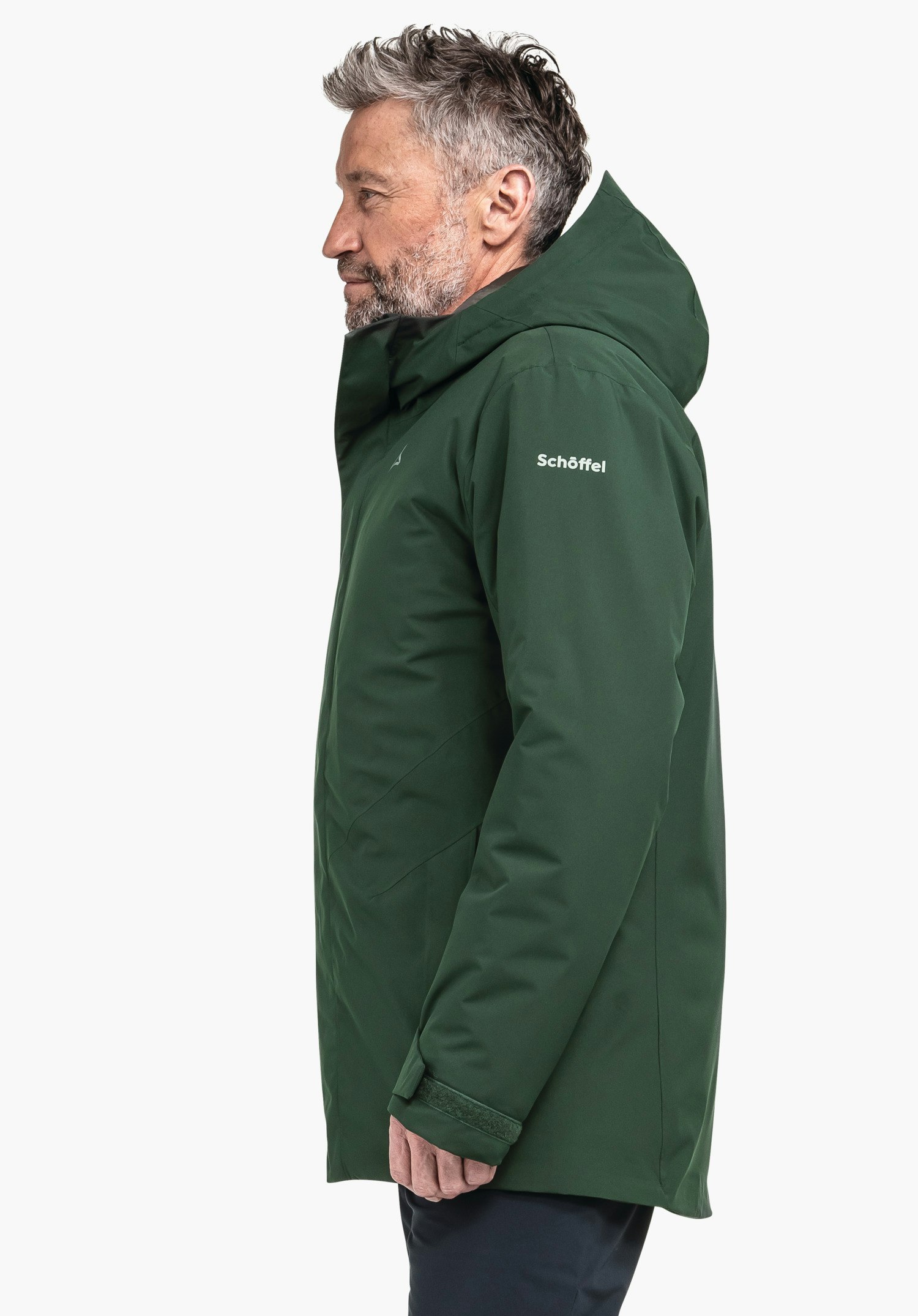 Parka Style Froda MNS dunkelgrüne Jacke, getragen von einem Mann im Profil, Kapuze hochgestellt, vor weißem Hintergrund. Auf dem Oberarm steht "Schöffel". Schöffel-Logo auf der Brust.