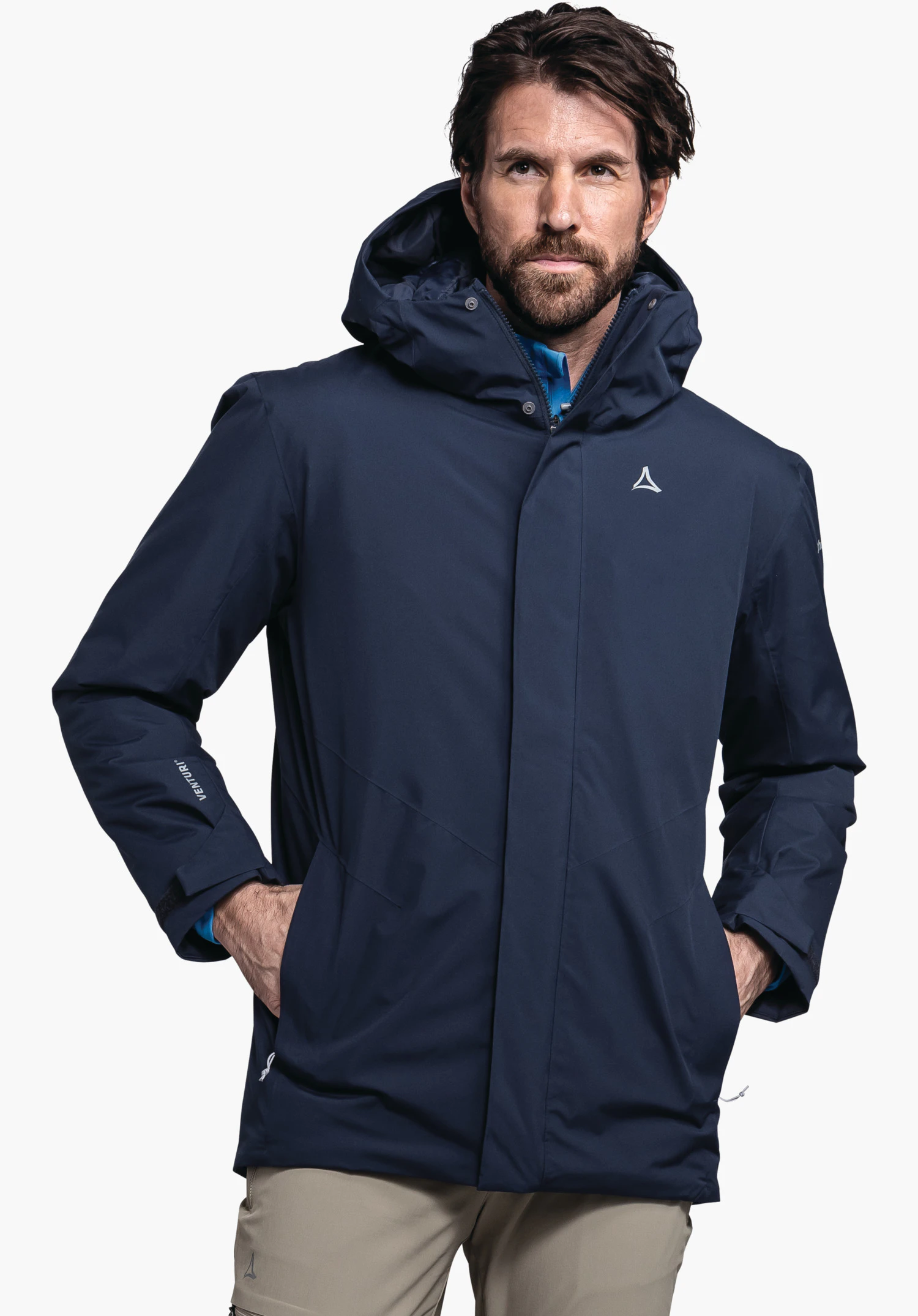 Parka Style Froda MNS in blue with Schöffel logo on the chest, worn by a male model standing upright with his hands in his pockets and shown from the front against a white background. (AI-generated)