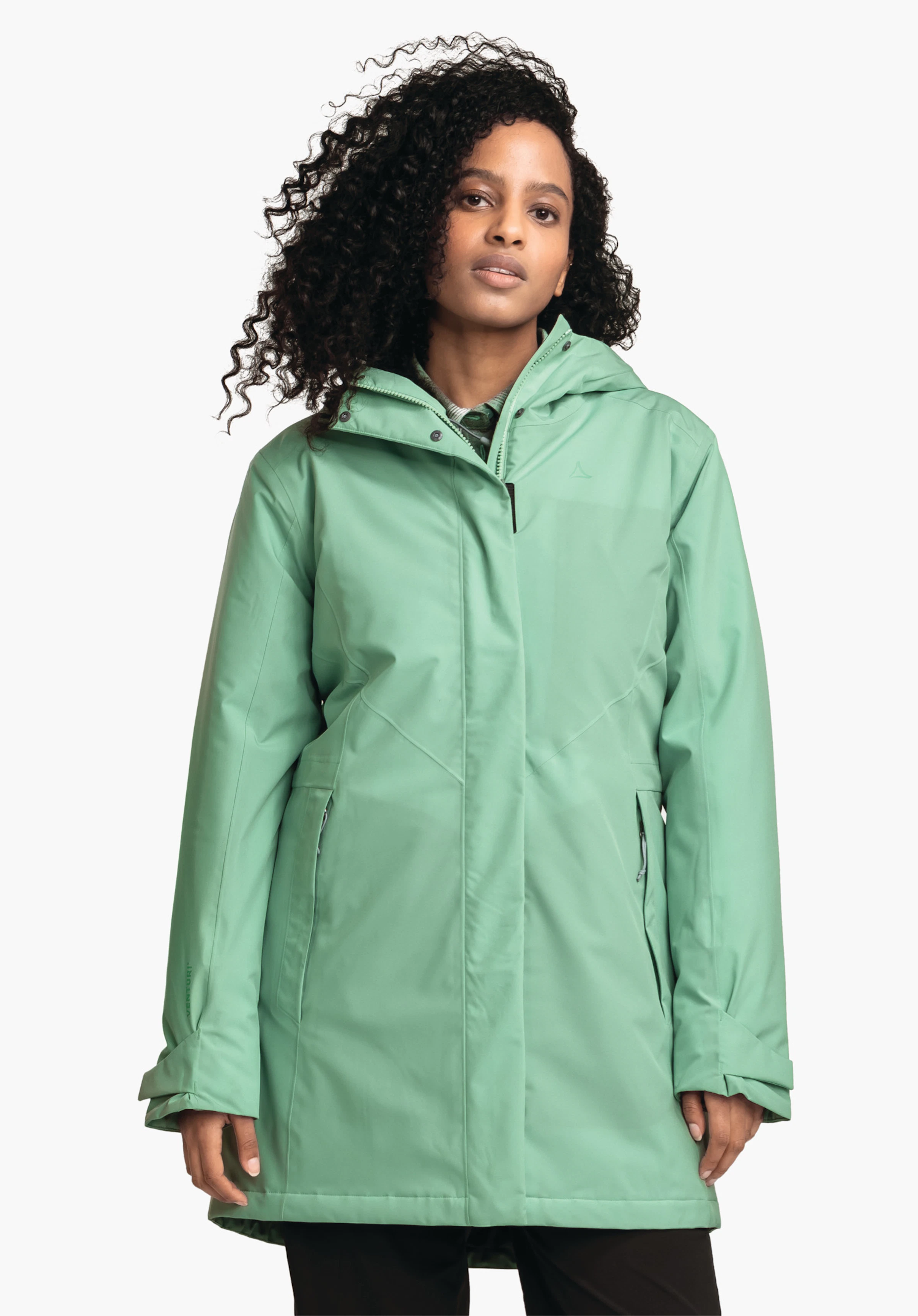 Parka Style Froda WMS Femme portant une parka vert clair à capuche, debout de face devant un fond clair; mains détendues le long du corps, pantalon noir visible; logo Schöffel sur la poitrine gauche.