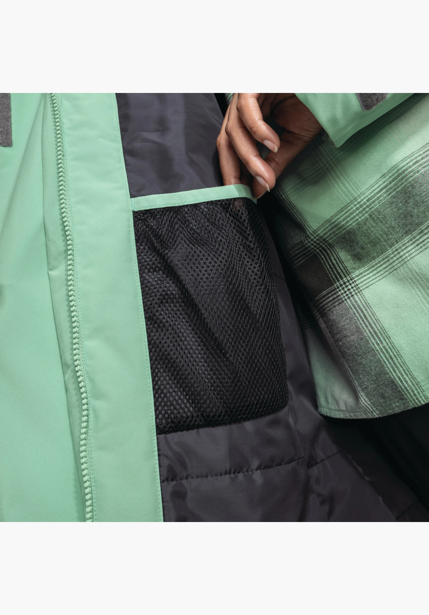 Parka Style Froda WMS présente une vue détaillée de l'intérieur avec une poche pratique en maille noire et la doublure à carreaux à côté du zip vert en gros plan sur fond blanc/neutre.