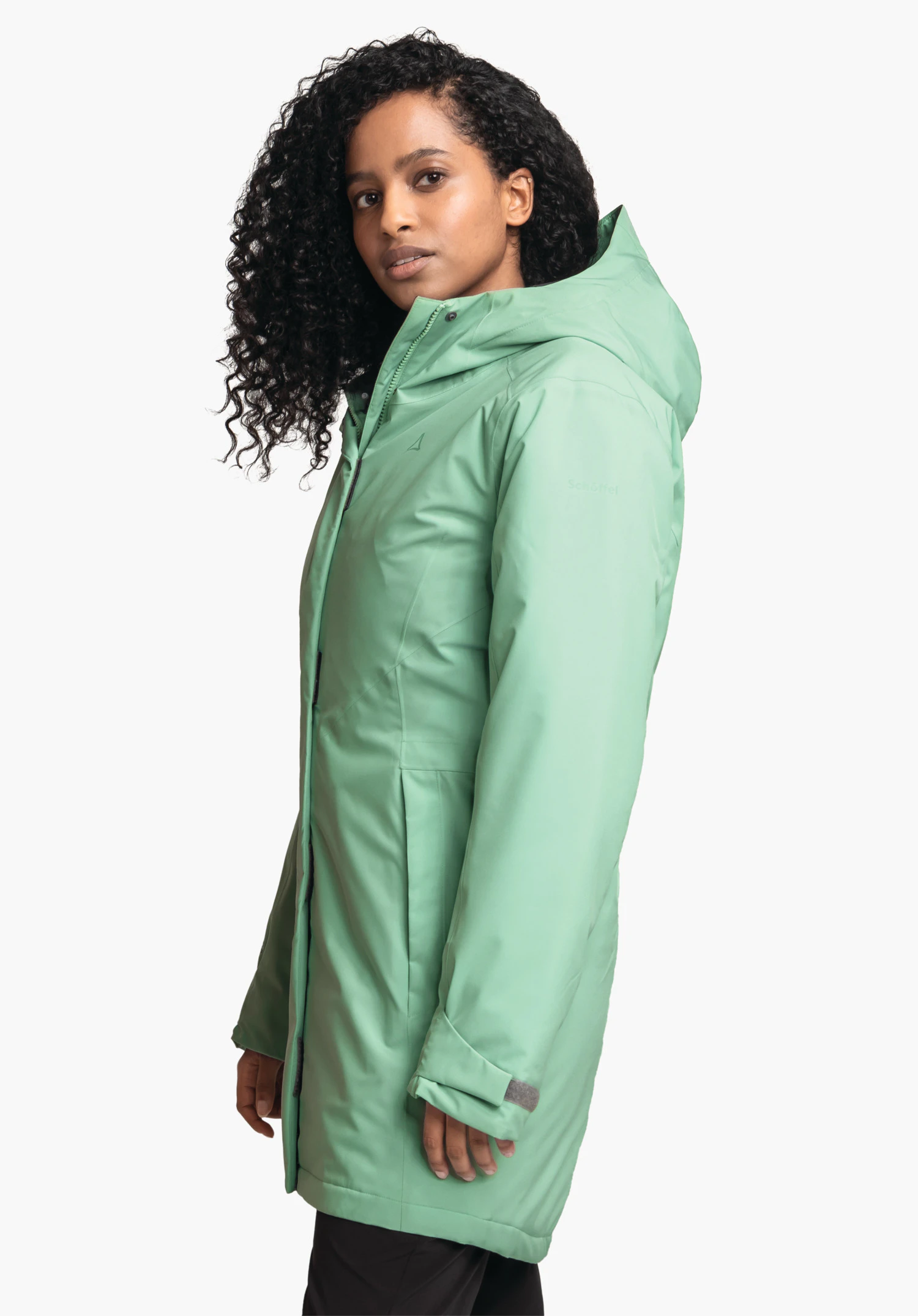 Parka Style Froda WMS veste vert clair à capuche portée de profil par une femme regardant la caméra devant fond blanc. Logo Schöffel visible; texte: "Schöffel".
