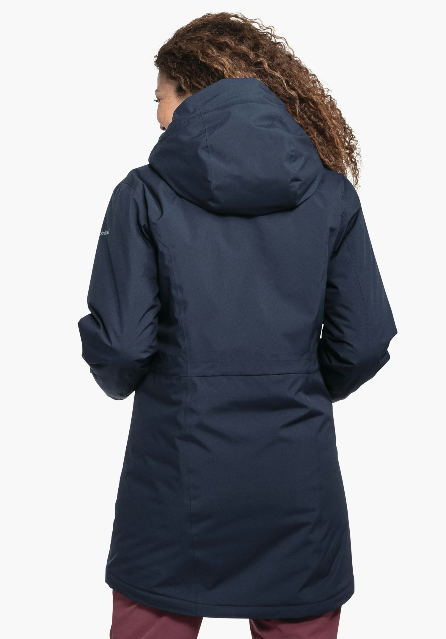 Parka Style Froda WMS parka bleu foncé, porté debout dos à la caméra, capuche relevée; personne devant un fond blanc neutre, pantalon rouge foncé visible. Aucun texte visible.