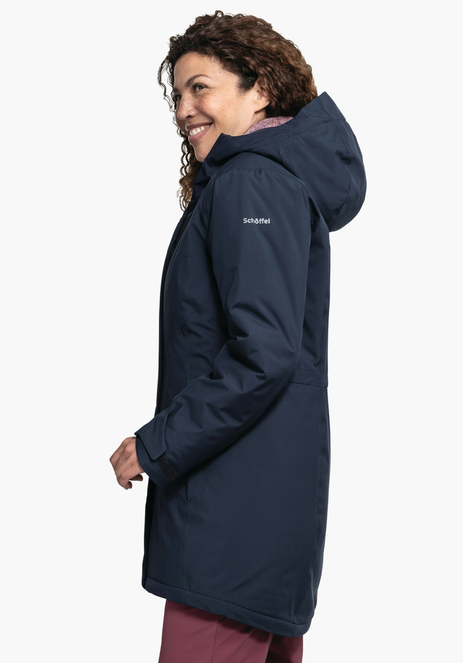 Parka Style Froda WMS veste bleu foncé portée de profil par une personne souriante regardant vers la gauche; fond blanc neutre; pantalon rouge visible. Texte sur la manche: "Schöffel".