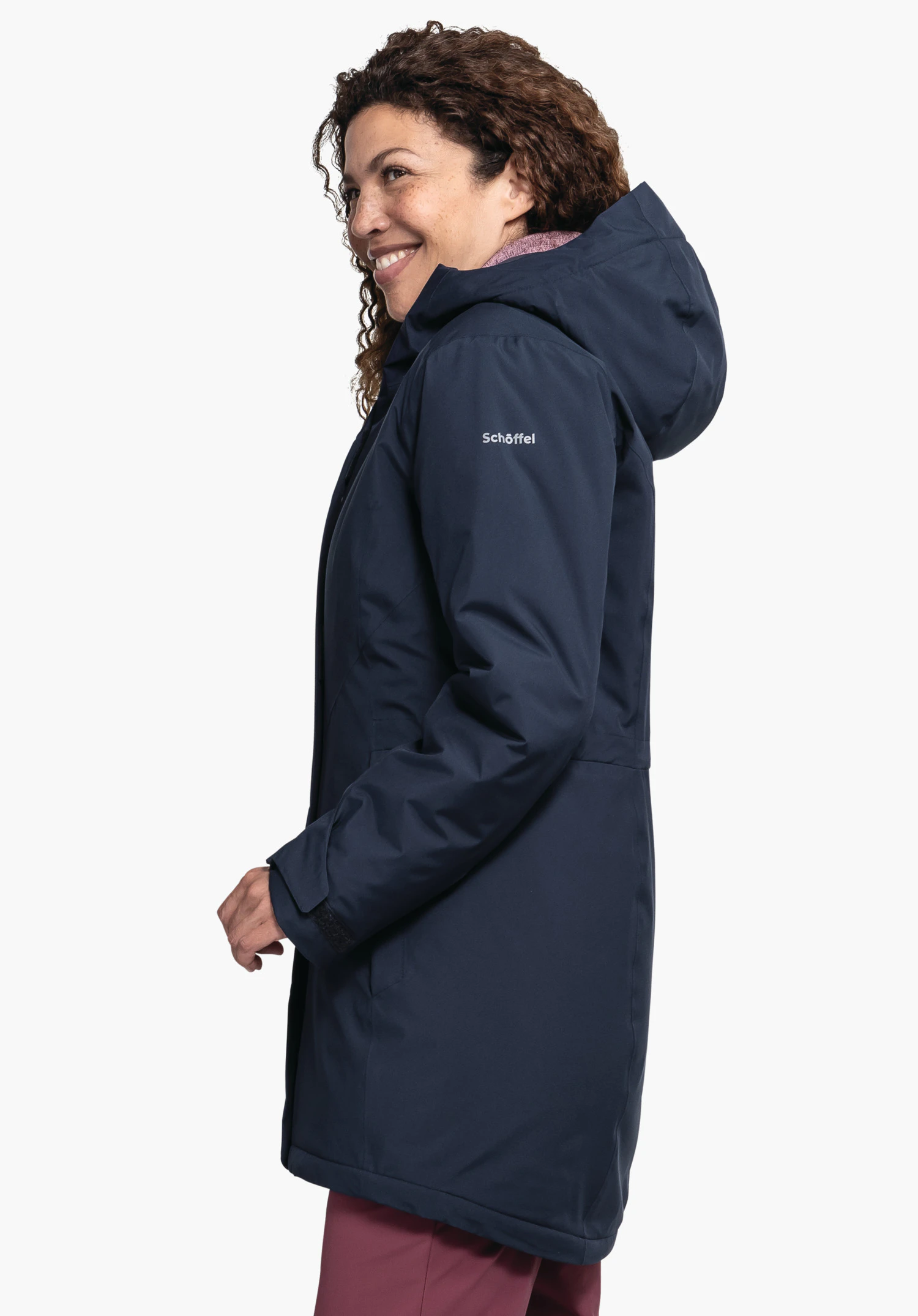 Parka Style Froda WMS veste bleu foncé portée de profil par une personne souriante regardant vers la gauche; fond blanc neutre; pantalon rouge visible. Texte sur la manche: "Schöffel".