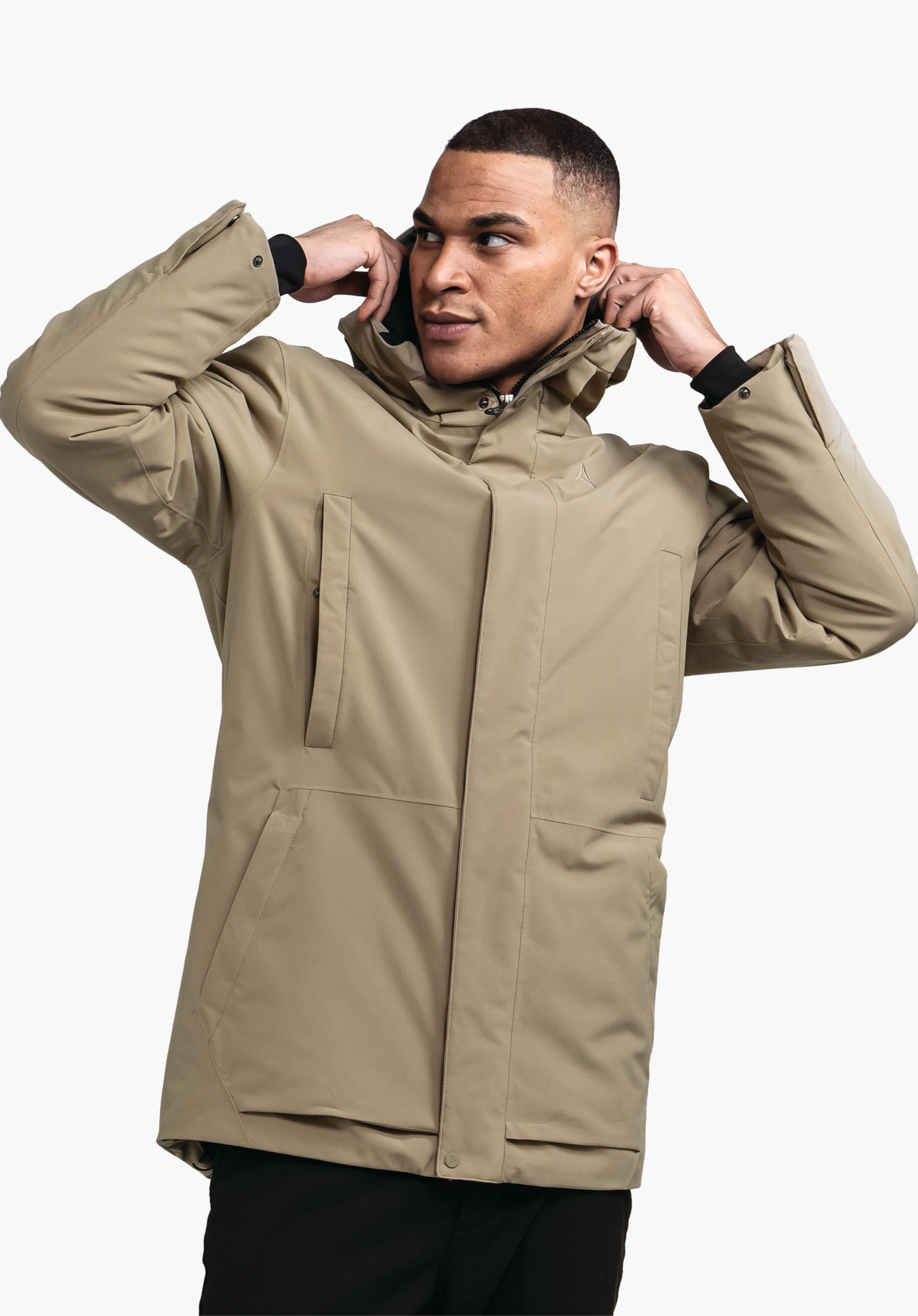 Ins Parka Style Crivat MNS hellgrüne Jacke mit Schöffel-Logo; Mann zieht Kapuze hoch, richtet sie am Hals; halbseitige Brustaufnahme vor einfarbigem hellem Hintergrund.