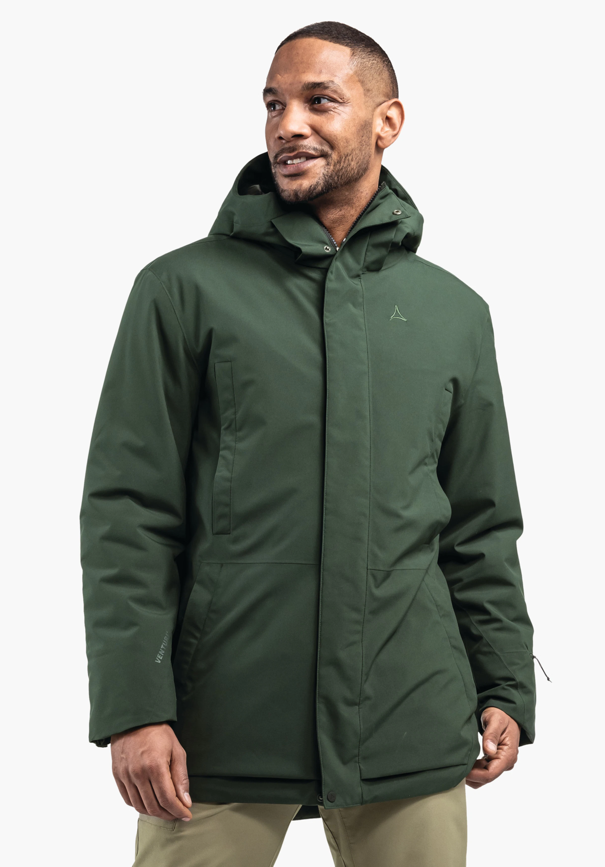 Ins Parka Style Crivat MNS parka vert foncé avec capuche et logo Schöffel, portée par un homme souriant regardant vers la droite, devant un fond clair et uni. Texte: «VENTURI».