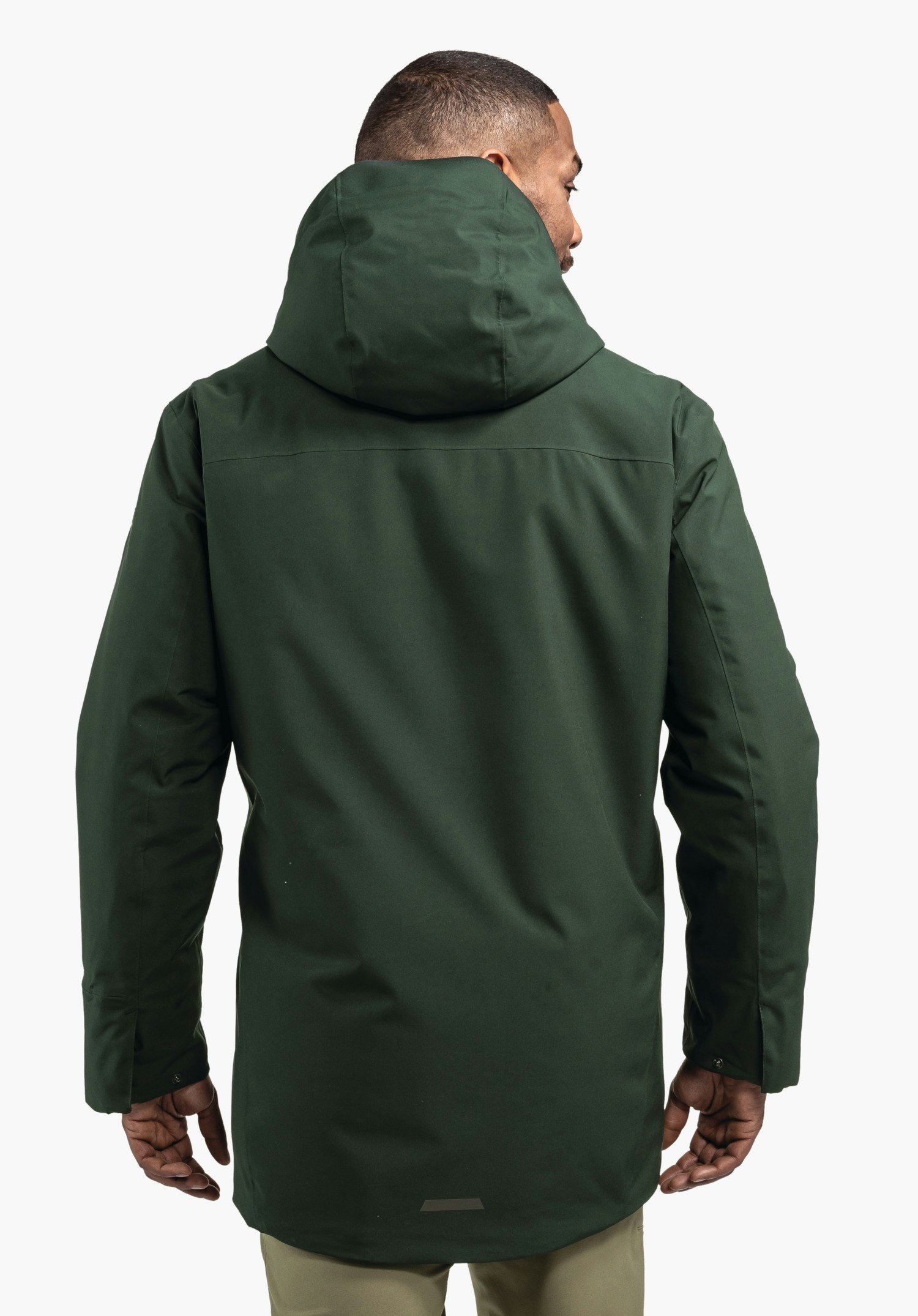 Ins Parka Style Crivat MNS Parka dunkelgrün, von einer Person getragen, steht mit dem Rücken zur Kamera, hochgestellte Kapuze, Arme locker seitlich, vor schlichtem weißem Hintergrund.