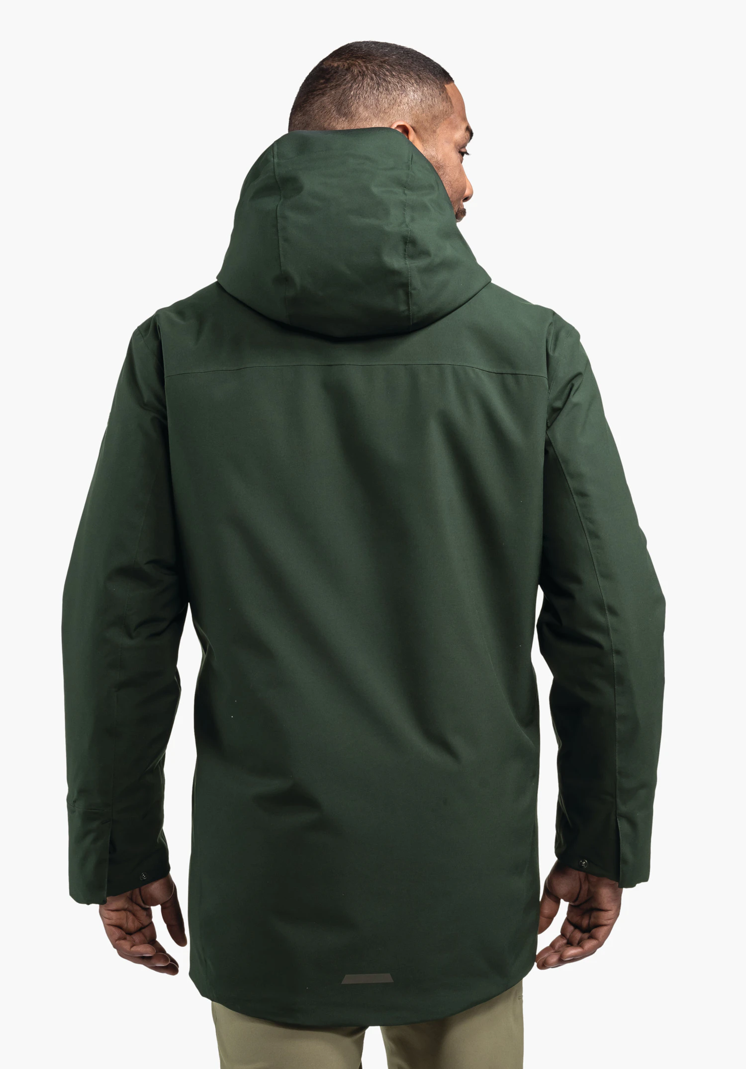 Ins Parka Style Crivat MNS Parka dunkelgrün, von einer Person getragen, steht mit dem Rücken zur Kamera, hochgestellte Kapuze, Arme locker seitlich, vor schlichtem weißem Hintergrund.