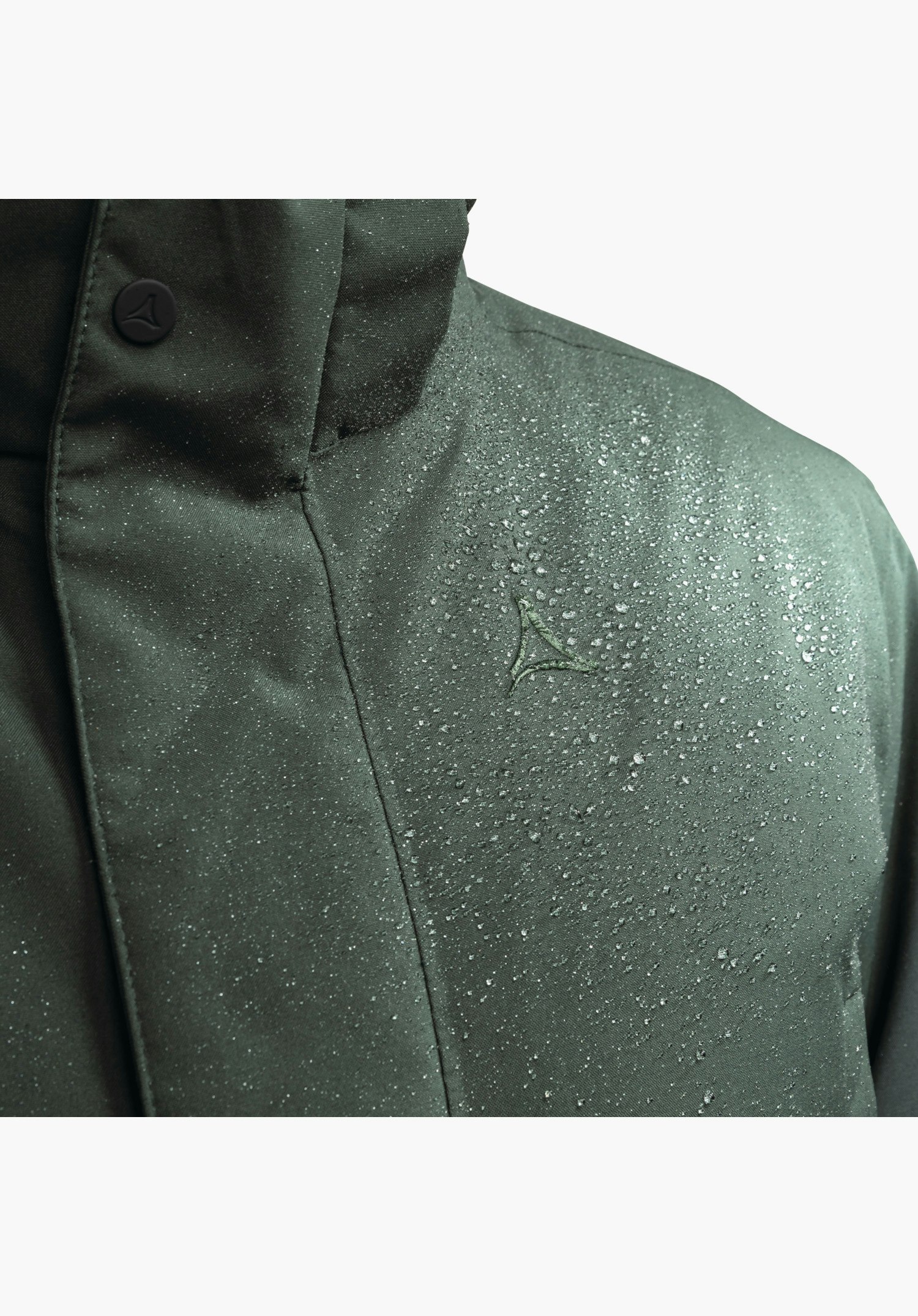 Ins Parka Style Crivat MNS zeigt die wasserabweisende Oberfläche des grünen Materials mit abperlenden Wassertropfen und das gestickte Schöffel-Logo auf der Brust, Nahaufnahme vor weißem Hintergrund.