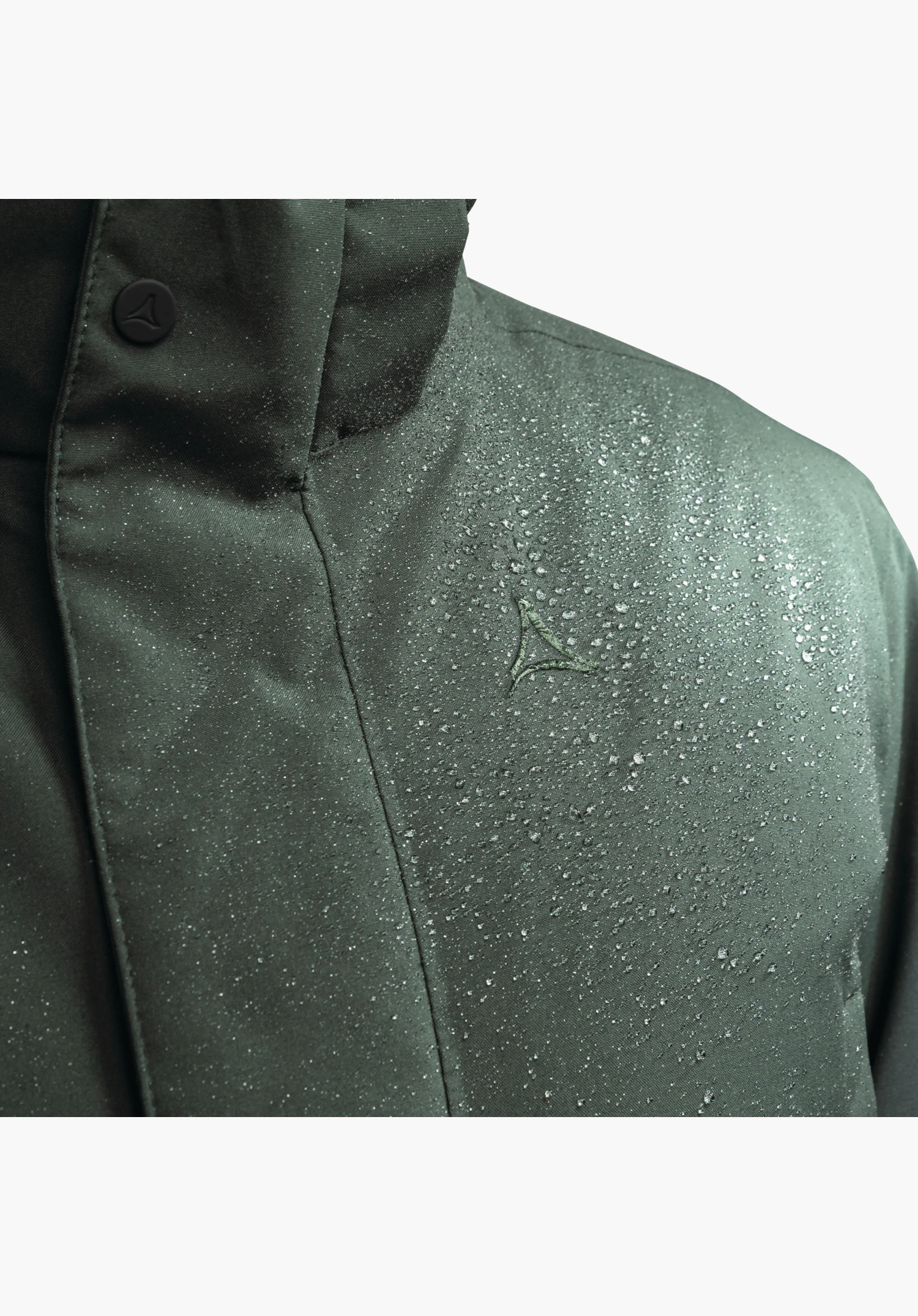 Ins Parka Style Crivat MNS zeigt die wasserabweisende Oberfläche des grünen Materials mit abperlenden Wassertropfen und das gestickte Schöffel-Logo auf der Brust, Nahaufnahme vor weißem Hintergrund.