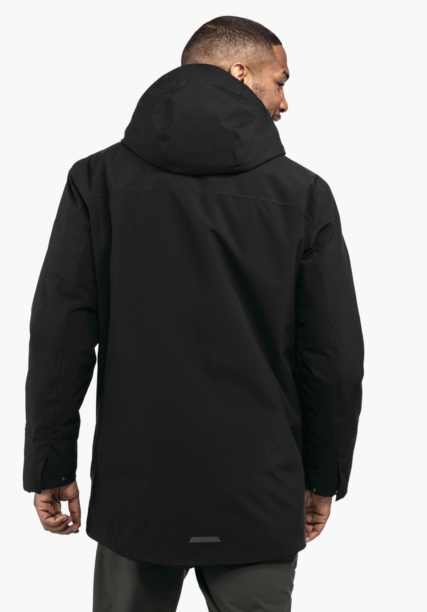 Ins Parka Style Crivat MNS Schwarze lange Kapuzenjacke, getragen von einem Mann, Rückenansicht; die Jacke hängt glatt und leicht ausgestellt. Heller weißer Hintergrund, dunkelgraue Hose, kleiner reflektierender Streifen am Saum.