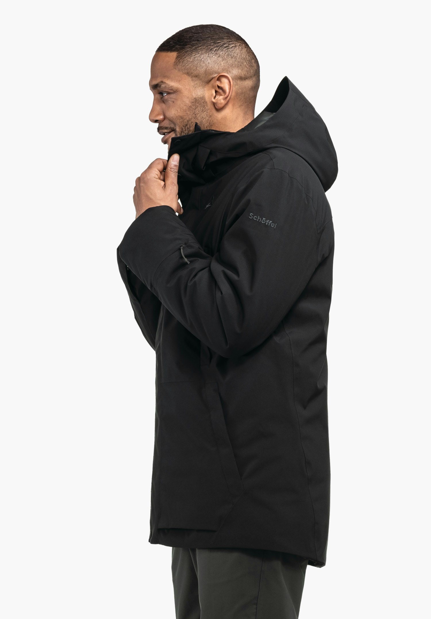 Ins Parka Style Crivat MNS schwarze Parka-Jacke, Mann zieht Kragen hoch; seitliche Aufnahme vor weißem Hintergrund. Text/Logo auf Ärmel: "Schöffel".