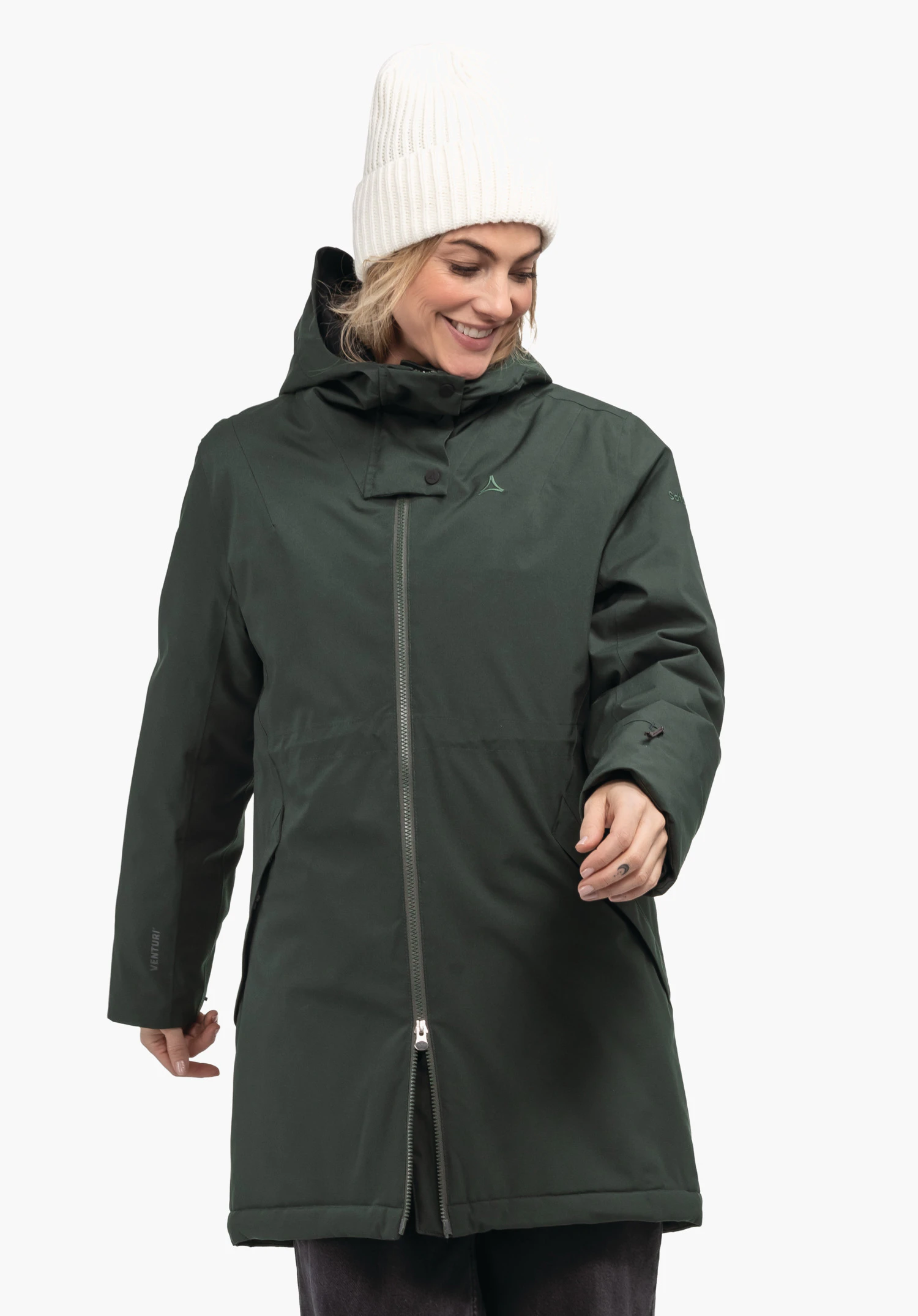 Ins Parka Style Crivat WMS Parka vert foncé avec logo Schöffel sur la poitrine, portée par une femme souriante avec un bonnet blanc cassé; elle regarde vers le bas et tend la main; fond clair. Texte sur la manche: VENTURI.