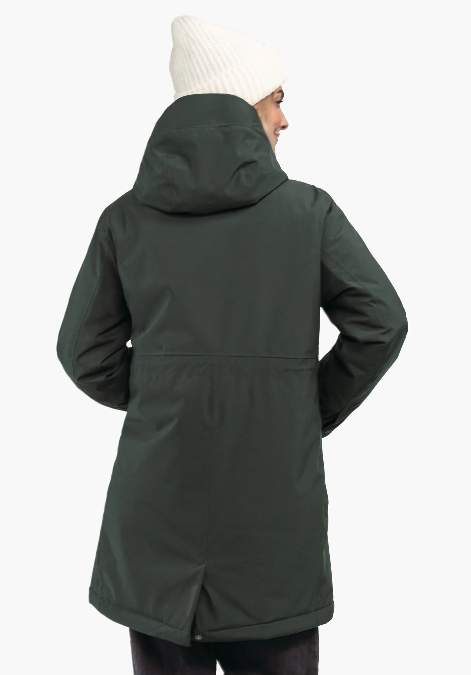 Ins Parka Style Crivat WMS dunkelgrüner, knielanger Parka; Person trägt ihn rückwärtsgewandt, Hände in Taschen, Kapuze aufgesetzt; weiße Strickmütze, leichtes Seitenprofil, vor hellem neutralem Hintergrund.