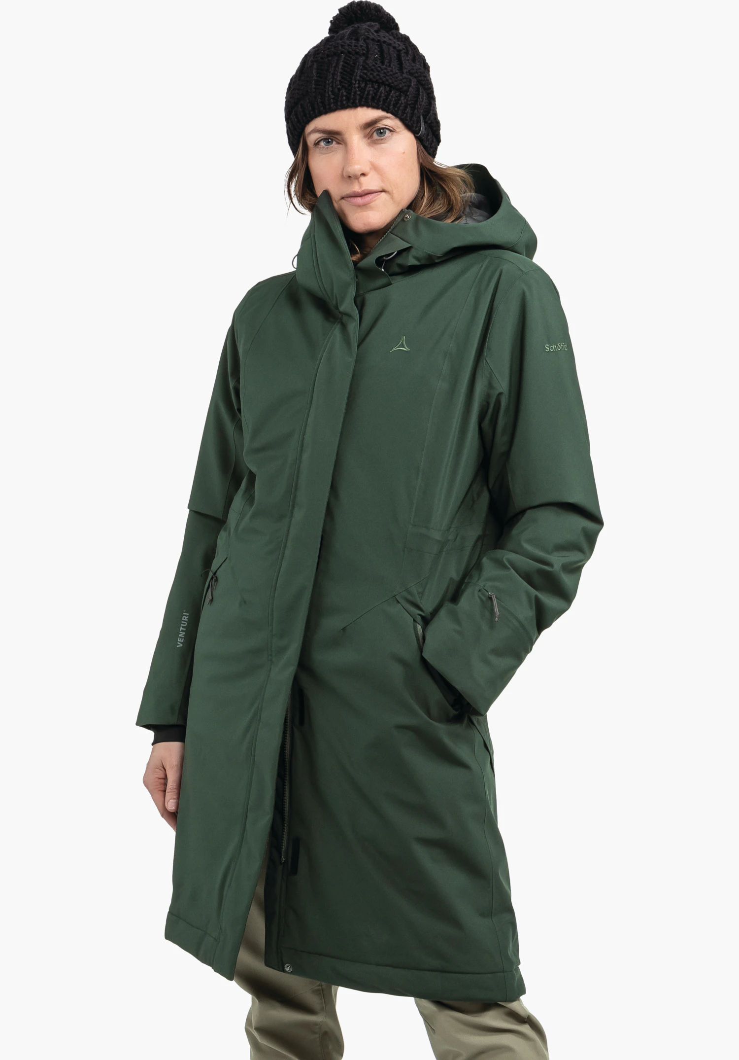Ins Coat Style Gregale WMS in grün, mit sichtbarem Schöffel-Logo auf der Brust, getragen von einem weiblichen Model im aufrechten Stand und Händen in den Taschen in Frontansicht vor weißem Hintergrund. (KI-generiert)