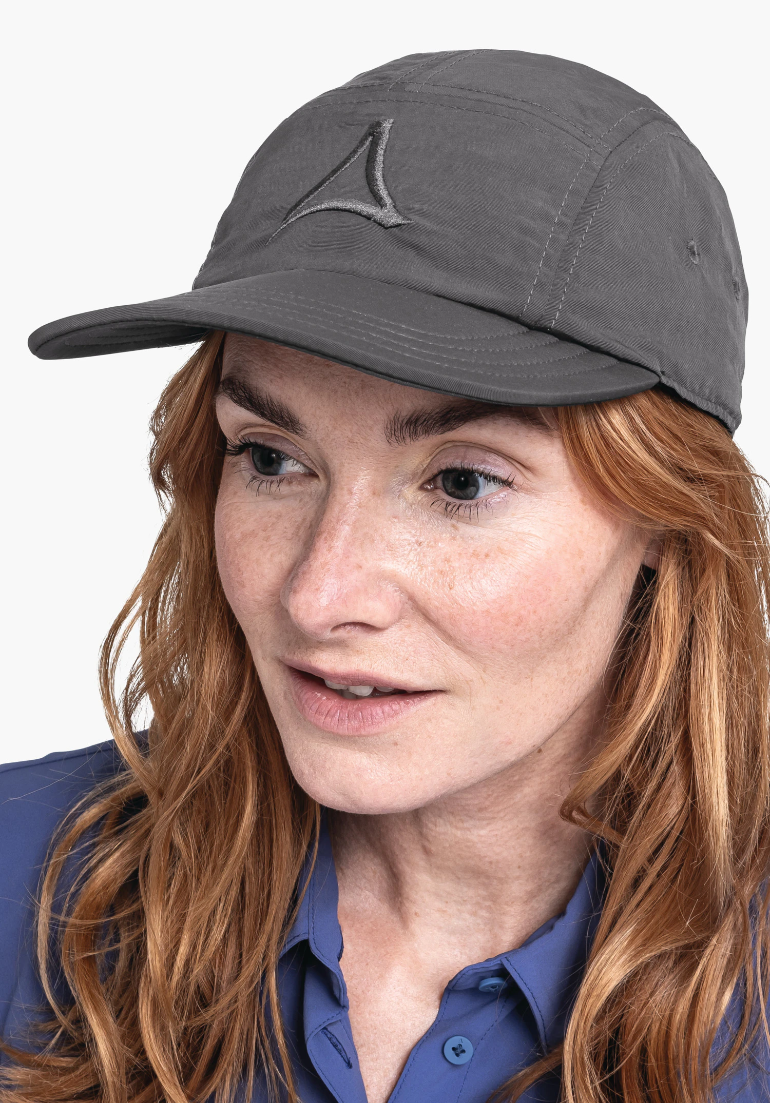 Sun Cap in grey, worn by a woman in a semi-profile pose, turning her head slightly to the side. The grey cap featuring the Schöffel logo on the front is displayed against a neutral background.