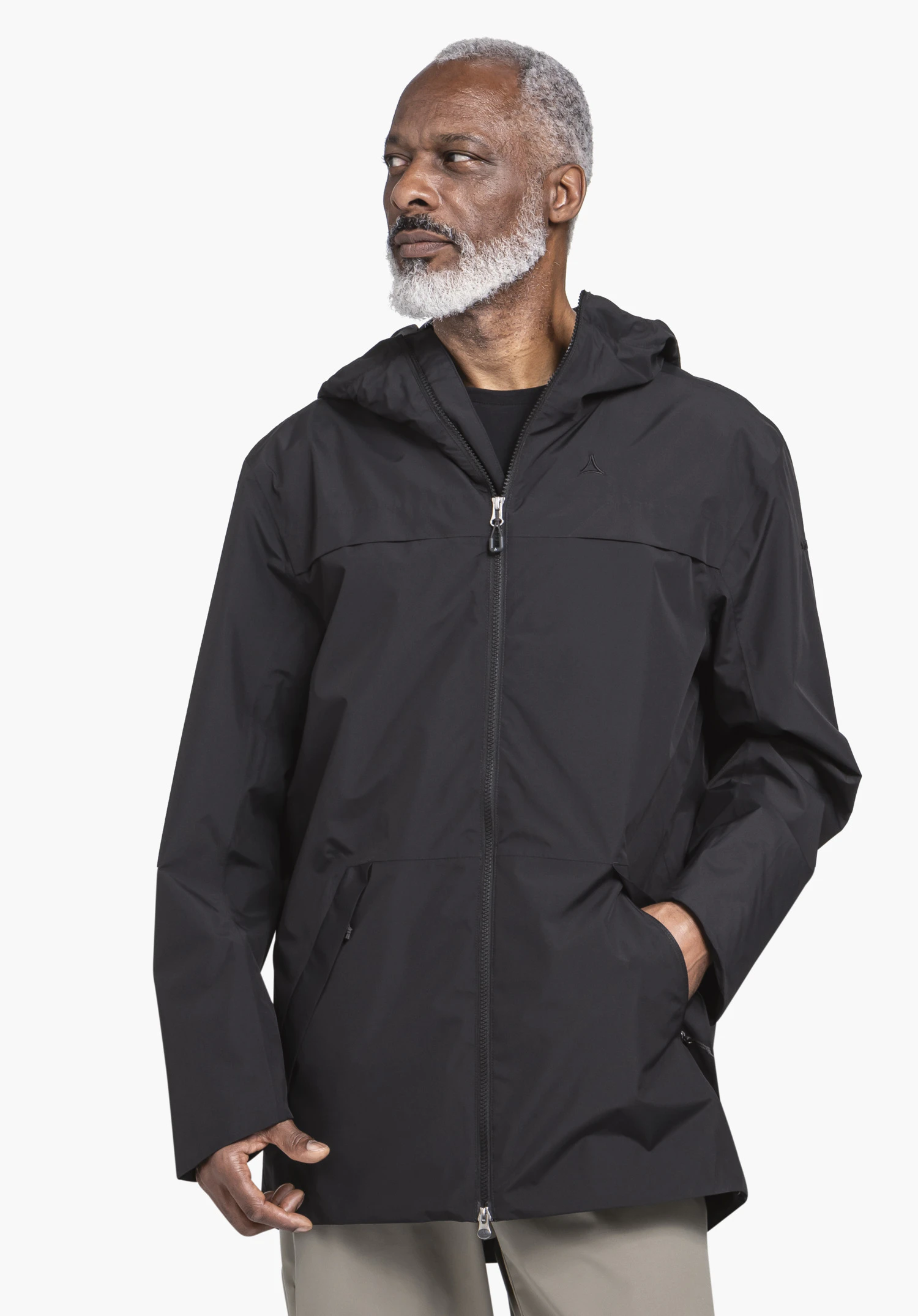 Parka Style Bohorok MNS porté par un mannequin qui se tient de face et regarde sur le côté, avec une main dans la poche de la veste. La parka noire montre le logo Schöffel sur la poitrine gauche et est présentée sur un fond neutre.