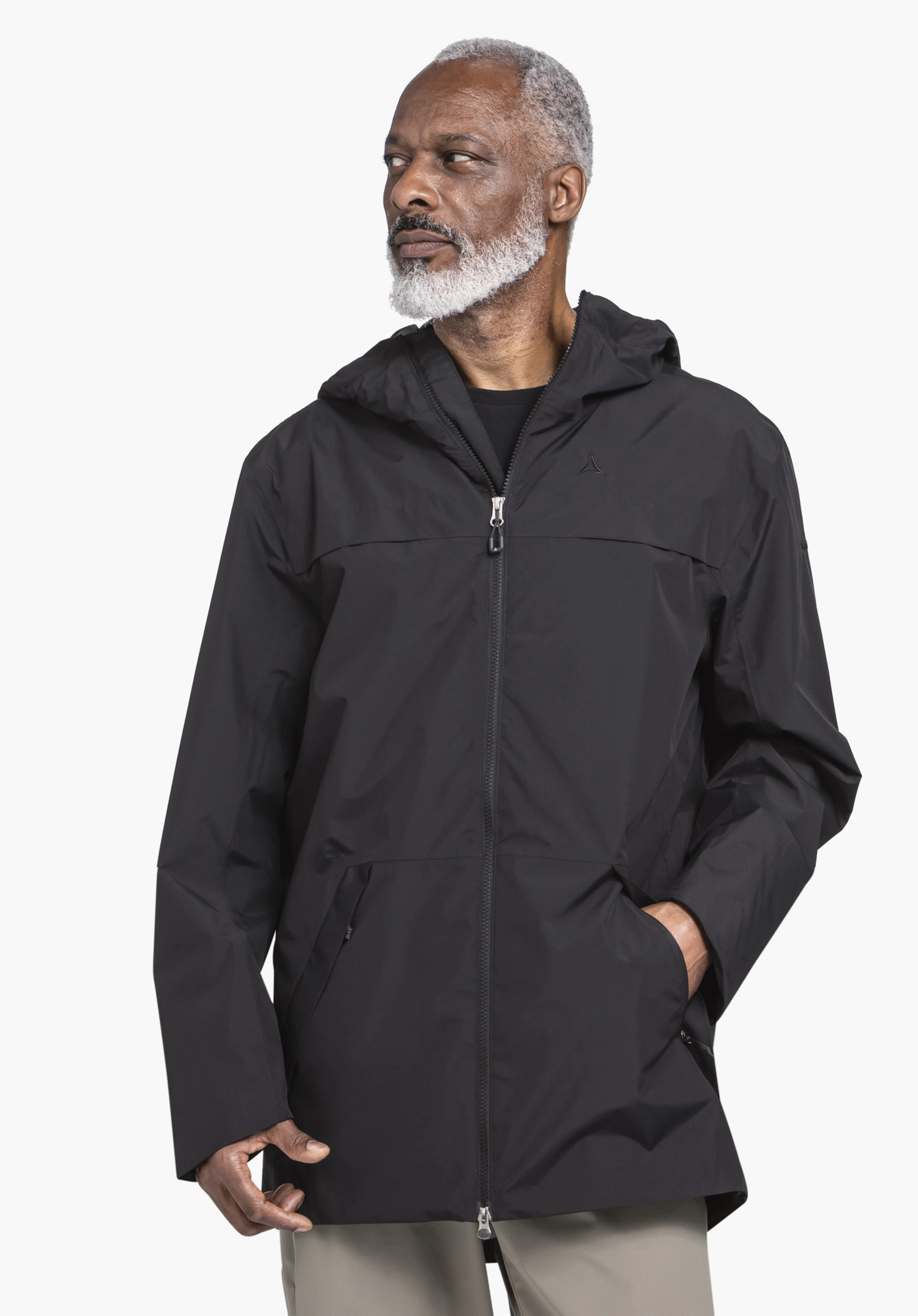 Parka Style Bohorok MNS gedragen door een model dat frontaal staat en opzij kijkt, met één hand in de jaszak. De zwarte parka toont het Schöffel-logo op de linkerborst en wordt gepresenteerd tegen een neutrale achtergrond.