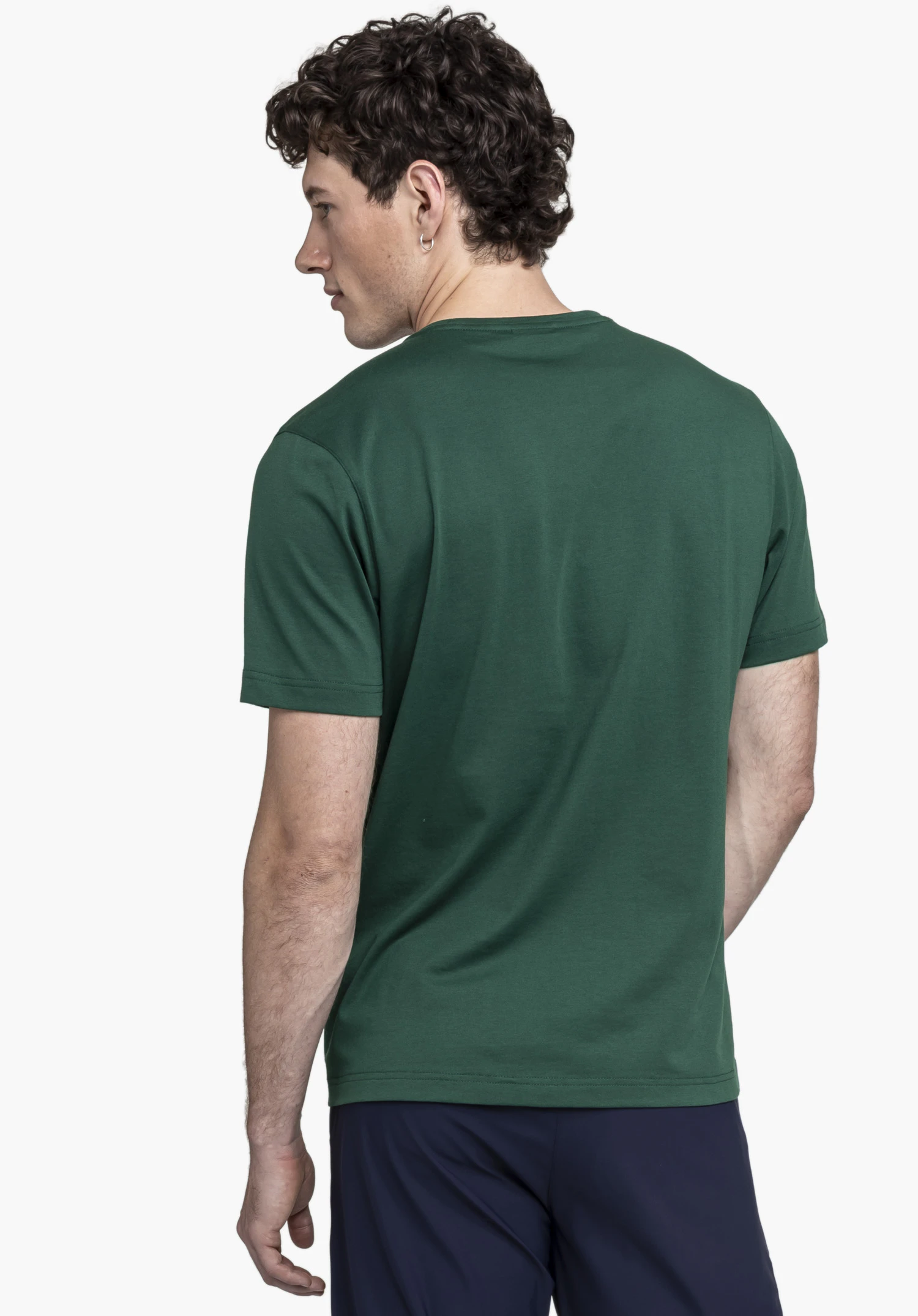T Shirt Style Collada MNS en vert : Vue de dos avec le modèle positionné légèrement de profil sur un fond neutre. Le t-shirt, dans un ton vert profond, souligne une allure épurée, agrémentée d'un discret logo Schöffel au niveau de l'ourlet.