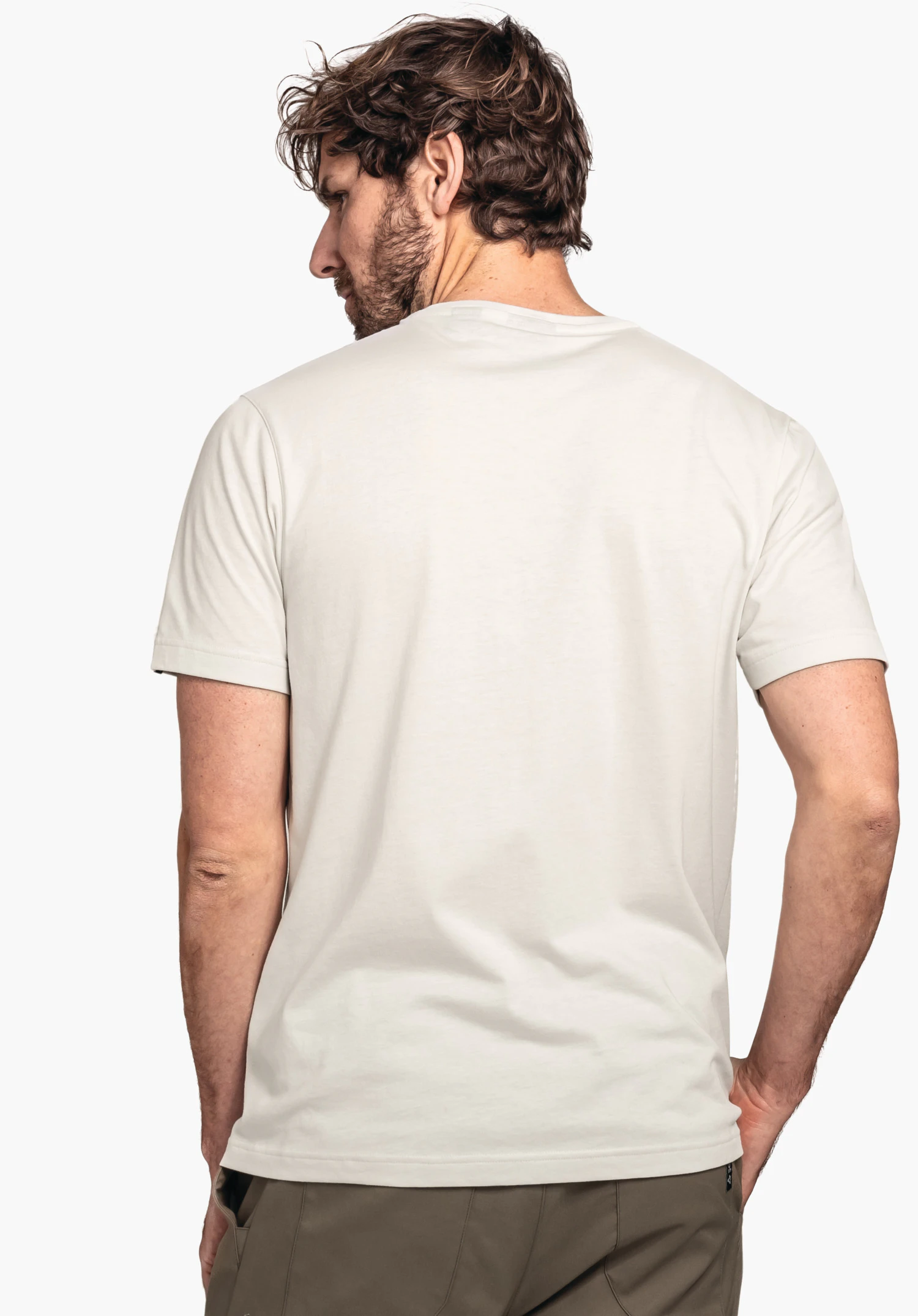 T Shirt Style Collada MNS lichtwit T-shirt, gedragen door een man met gedraaide romp die over de schouder kijkt; donkergroene broek, witte achtergrond.