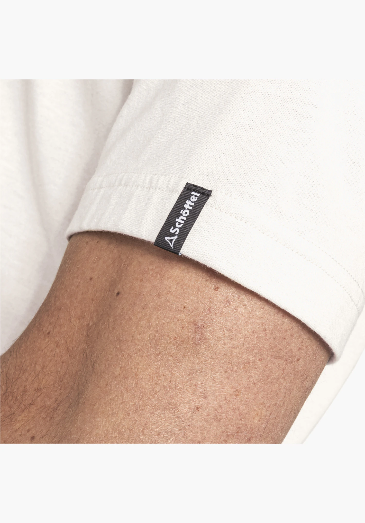 T Shirt Style Collada MNS toont het zwarte geweven label met wit Schöffel-logo aan de mouwzoom van de natuurkleurige stof als close-up voor een witte achtergrond.