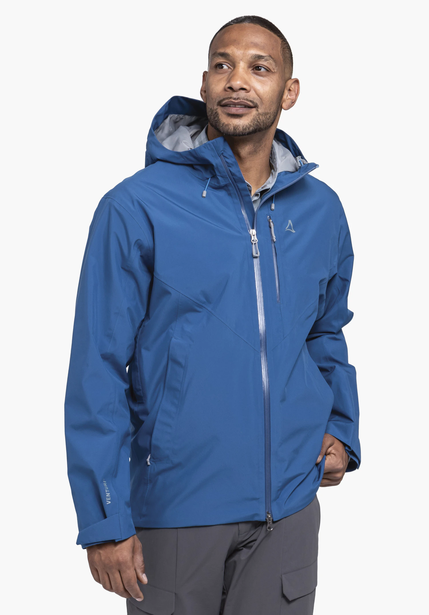 Jacket Style Mauku MNS getragen von einem Model, das leicht seitlich steht. Man sieht die Jacke in der Farbe Blau mit Kapuze, Frontreißverschluss und dem Schöffel-Logo auf der linken Brust vor einem neutralen Hintergrund.