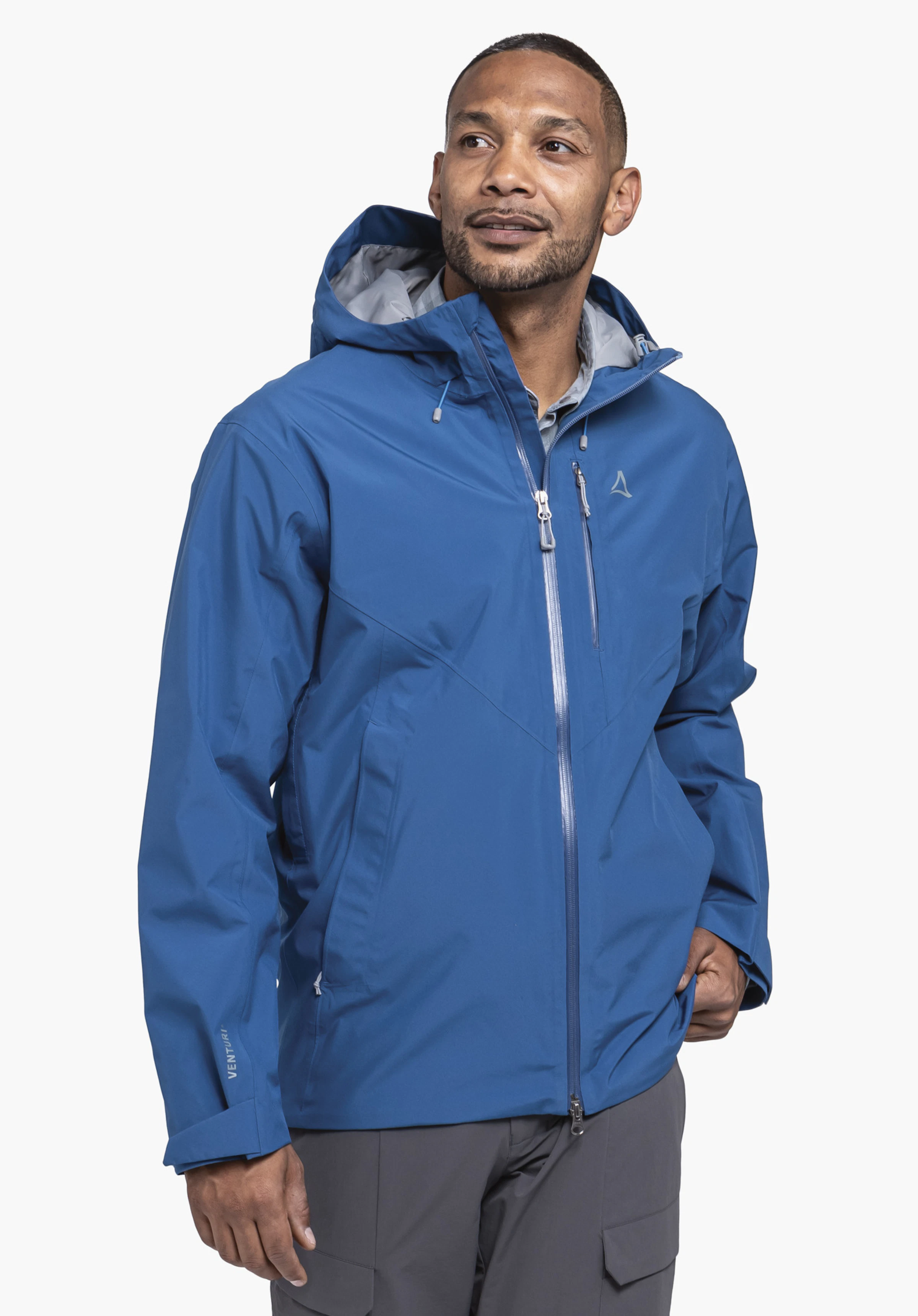 Jacket Style Mauku MNS getragen von einem Model, das leicht seitlich steht. Man sieht die Jacke in der Farbe Blau mit Kapuze, Frontreißverschluss und dem Schöffel-Logo auf der linken Brust vor einem neutralen Hintergrund.