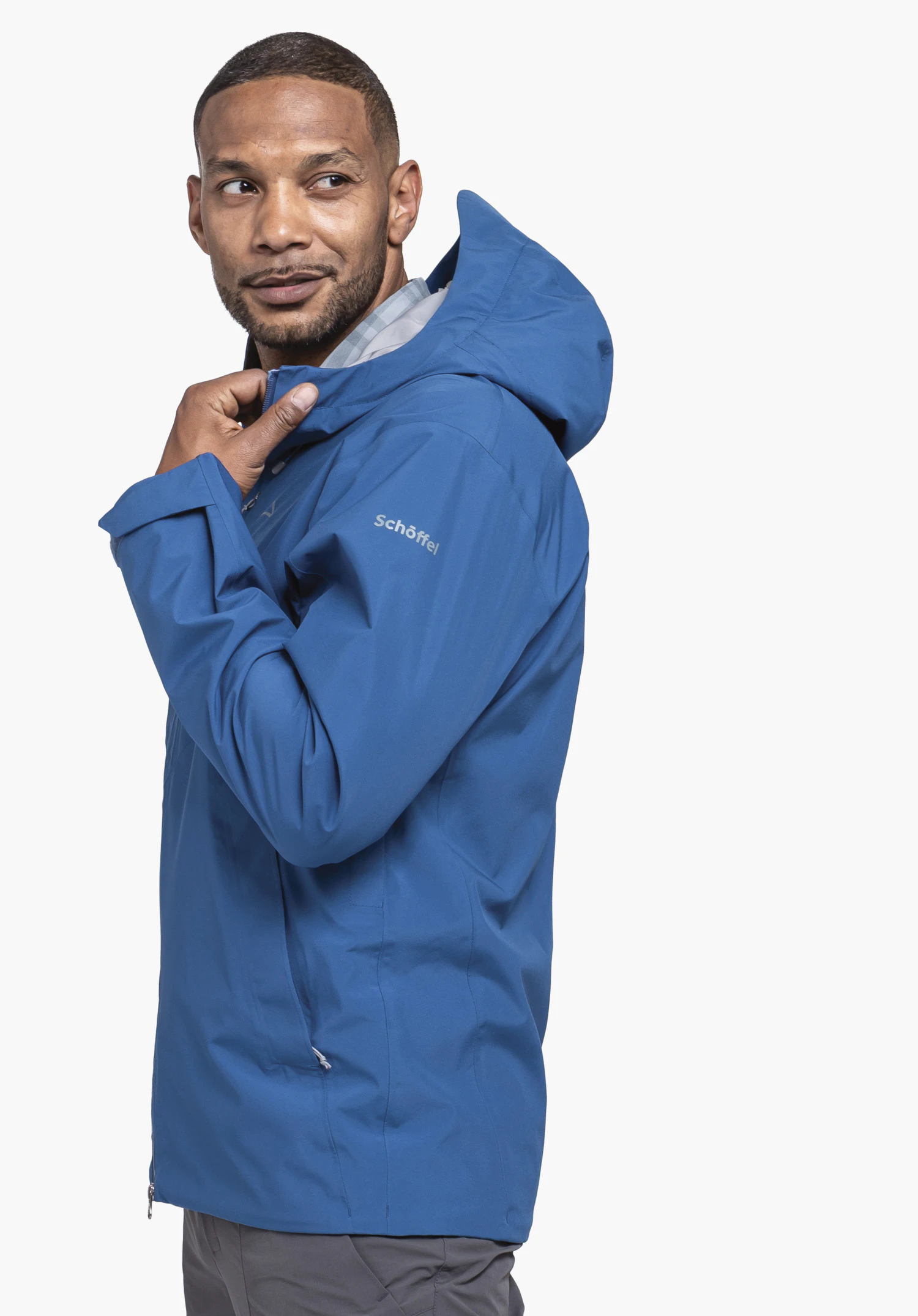 Jacket Style Mauku MNS in der Farbe Blau. Das Model steht seitlich, blickt über die Schulter und hält den Kragen der Jacke. Das Schöffel-Logo ist auf dem linken Ärmel sichtbar, präsentiert vor einem neutralen Hintergrund.