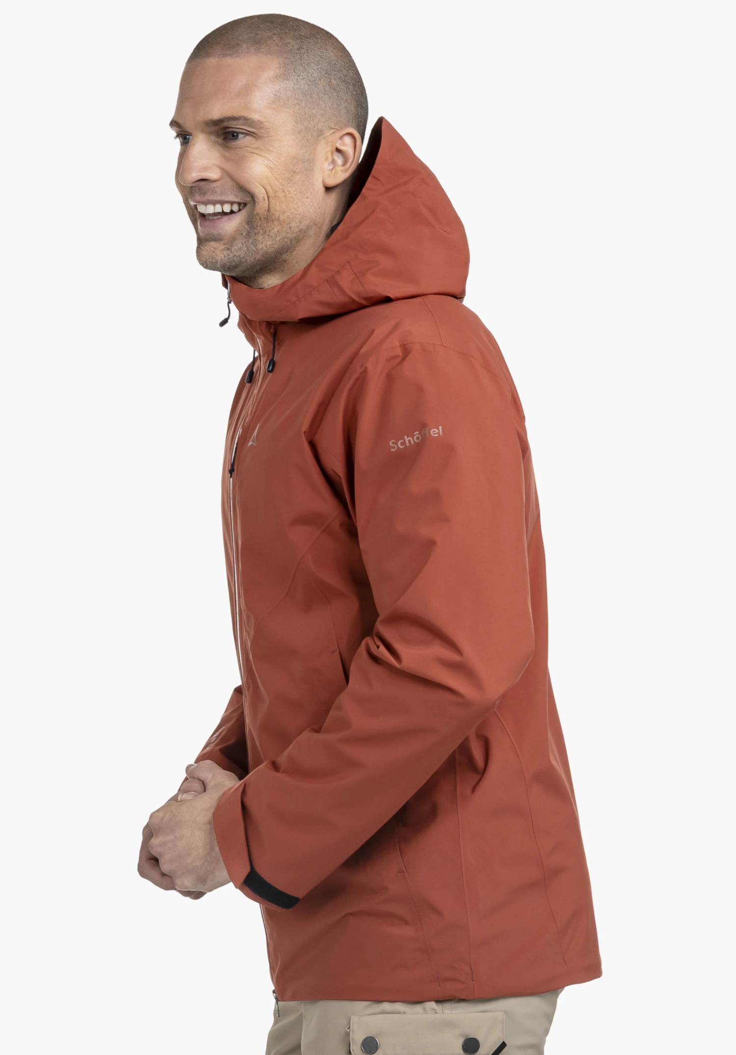 Jacket Style Mauku MNS. Een lachend model staat zijwaarts en draagt de rode jas met een goed zichtbaar Schöffel-Logo op de bovenarm tegen een neutrale achtergrond.