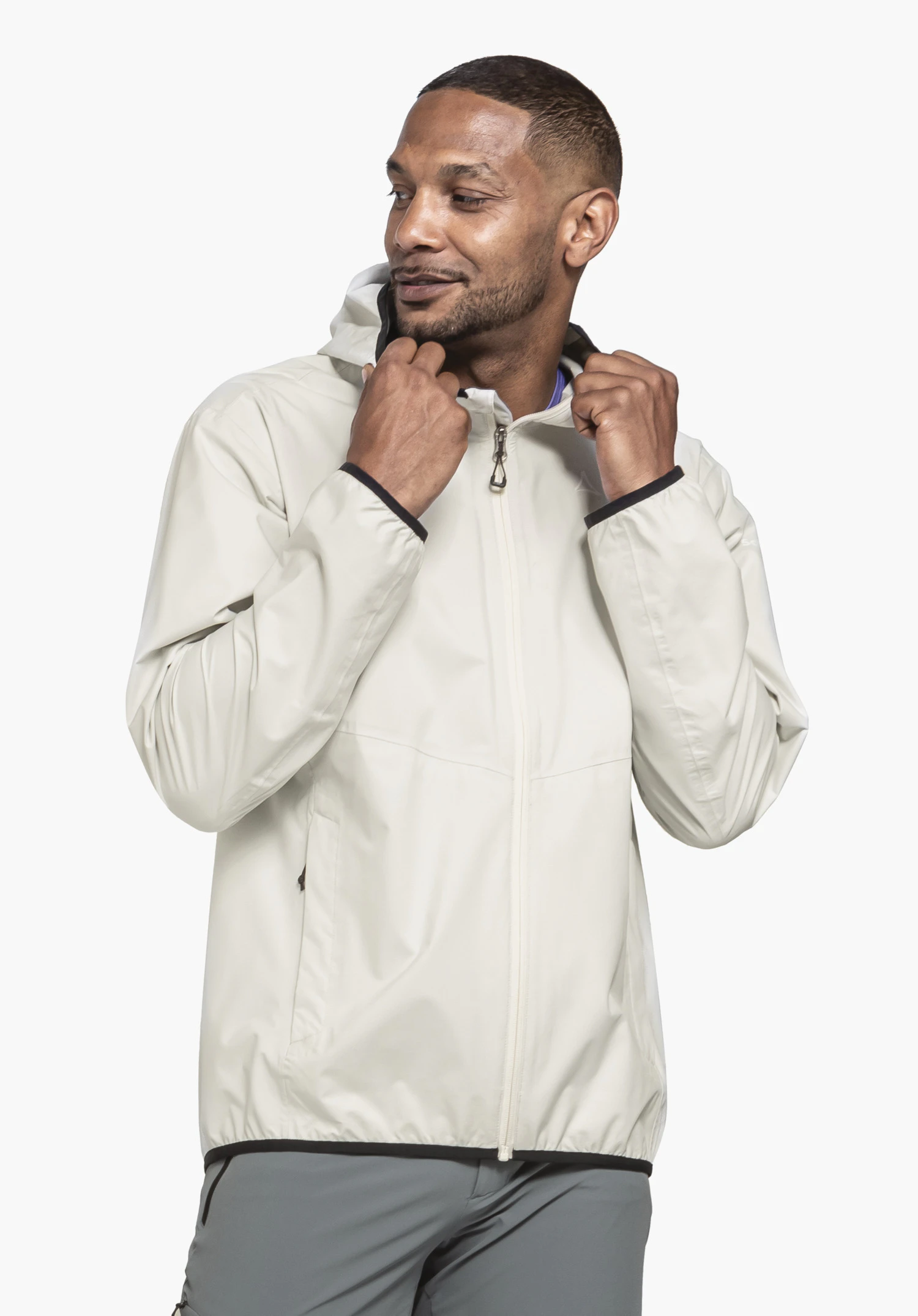 Jacket Style Migandi MNS an einem Model, das frontal steht und den Blick zur Seite richtet. Die Hände greifen den Kragen der Jacke in der Farbe Natur, auf deren Brust ein dezentes Schöffel-Logo sichtbar ist, fotografiert vor einem neutralen Hintergrund.
