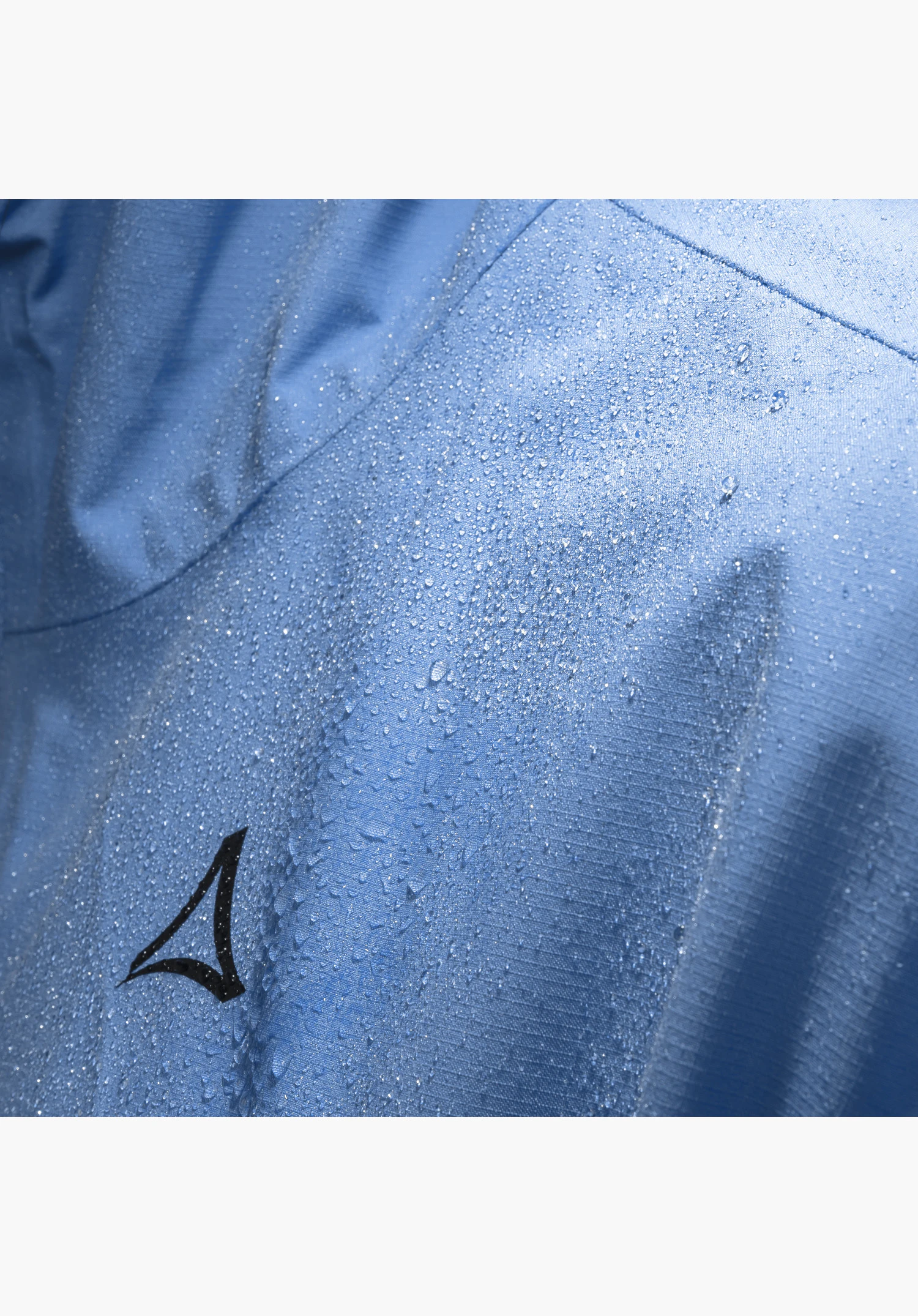 Jacket Style Migandi MNS, Detail des blauen Stoffes mit abperlenden Wassertropfen und schwarzem Schöffel-Logo, Nahaufnahme vor weißem/neutralem Hintergrund.