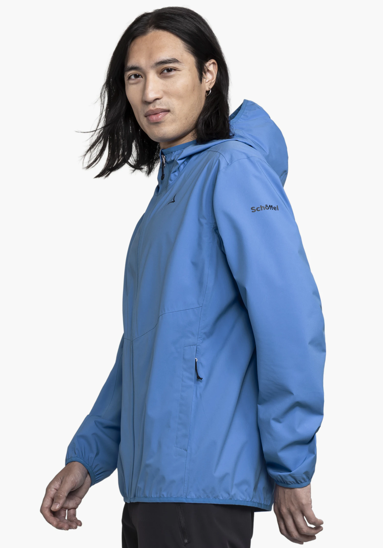 Jacket Style Migandi MNS in Blau, getragen von einem Model, das seitlich steht. Man sieht die Jacke mit dem sichtbaren Schöffel-Logo auf dem Ärmel und der Brust, aufgenommen vor einem neutralen Hintergrund.