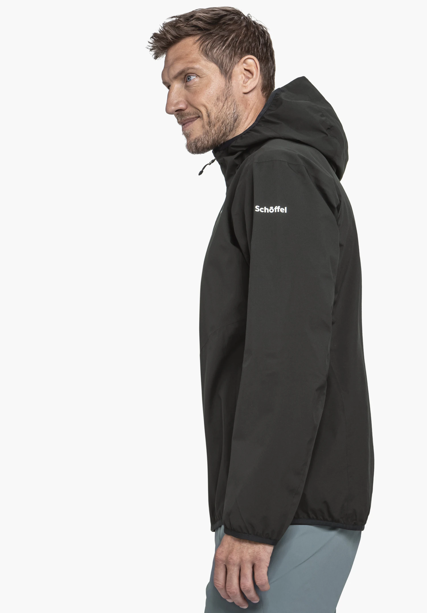 Jacket Style Migandi MNS black jacket worn by a man standing side-on and looking to the left; sleeve labelled "Schöffel"; light blue trousers; white background.