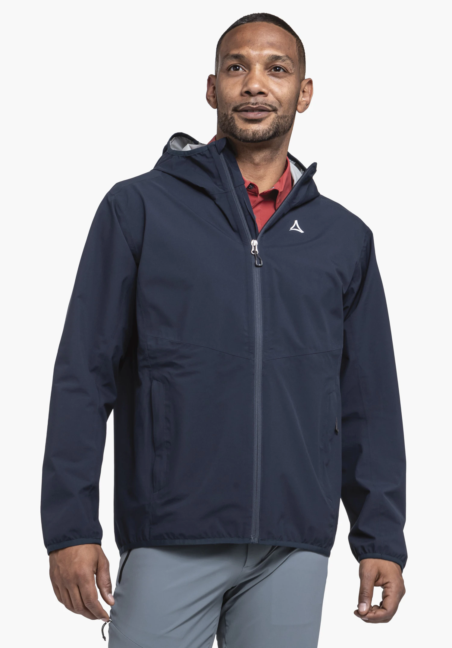 Jacket Style Migandi MNS Dark blue rain jacket with Schöffel logo, worn by a man looking slightly upwards to the right; red shirt visible, light blue trousers, neutral light background.