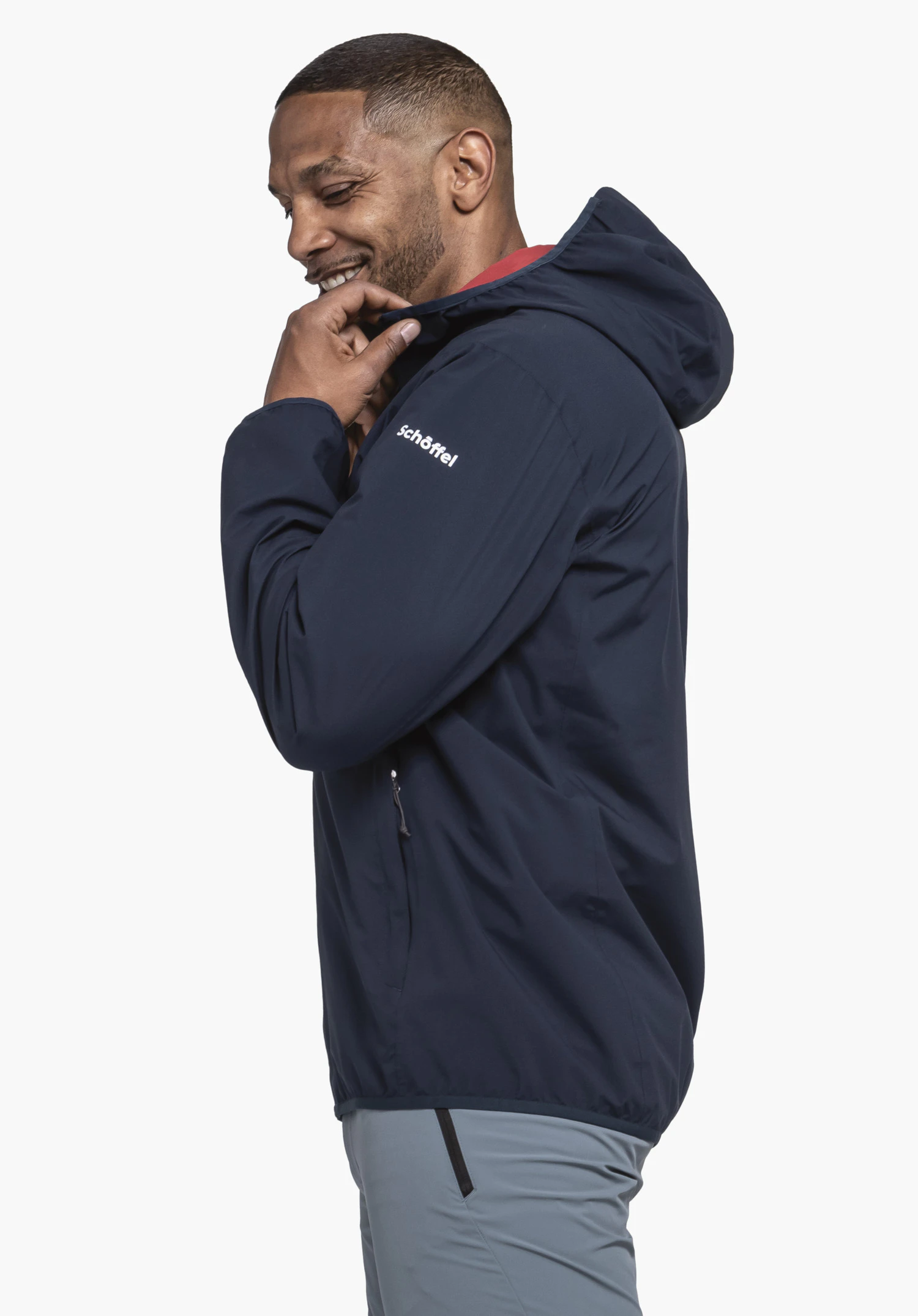 Jacket Style Migandi MNS dark blue jacket; man pulls the collar up, stands side-on in front of a white background; sleeve text: "Schöffel"; wears light blue trousers.
