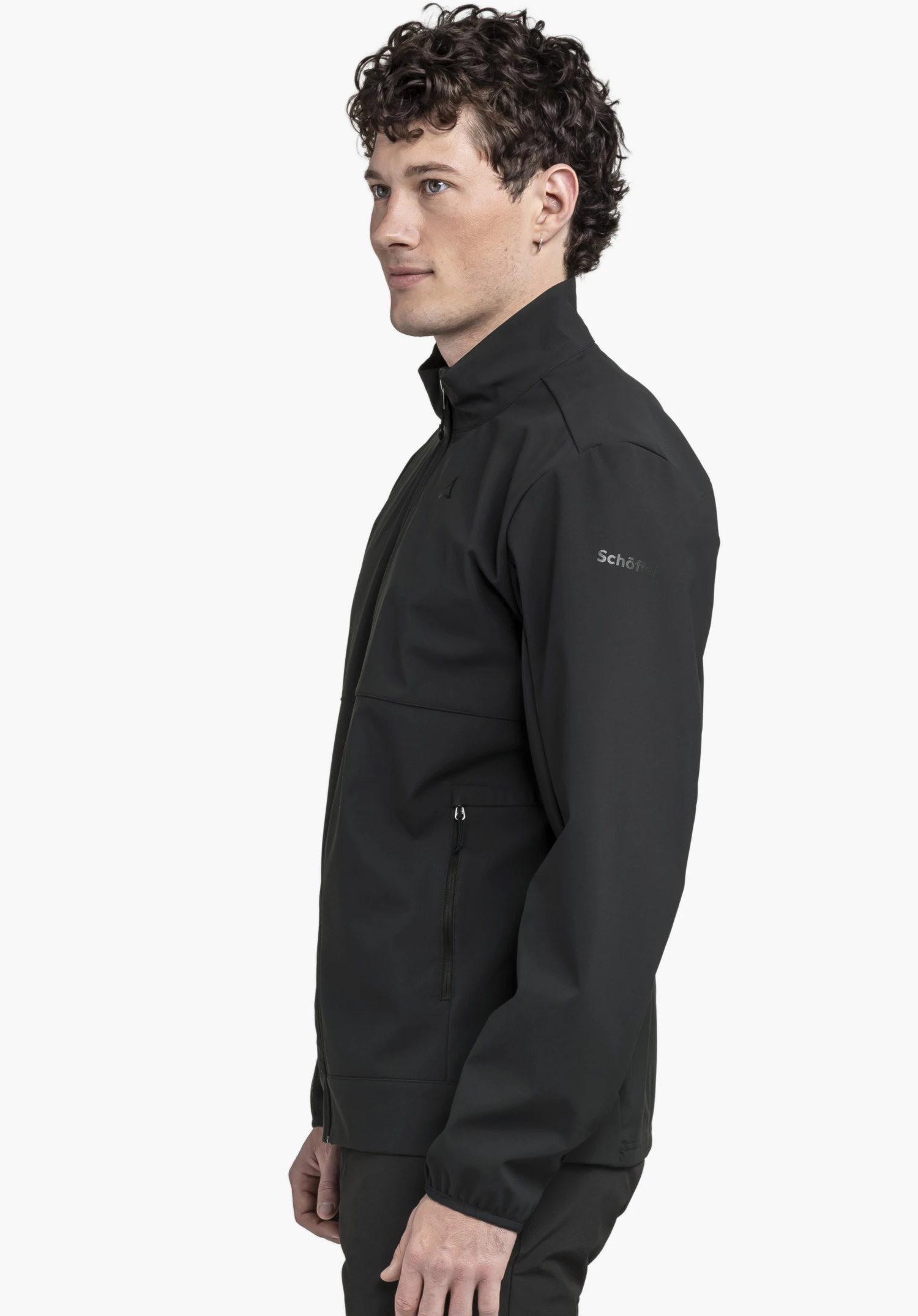 Softshell Jk Style Mirusha MNS portée par un mannequin se tenant de profil. La veste de couleur noire laisse voir le logo Schöffel sur la manche gauche, présentée sur un fond neutre.