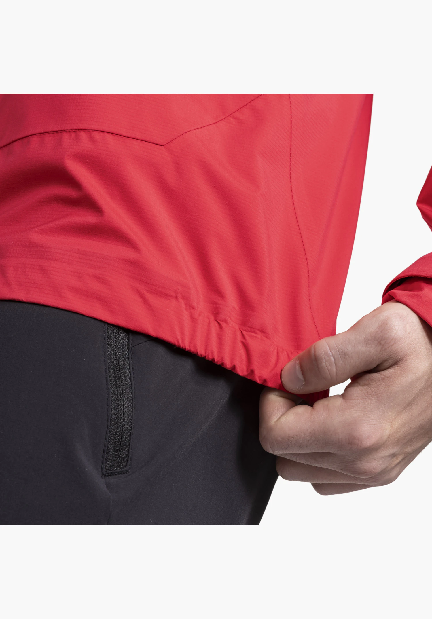 2.5L 3D Jacket Vistdal M, une main saisissant l'ourlet élastique du tissu rouge, gros plan sur fond blanc/neutre.