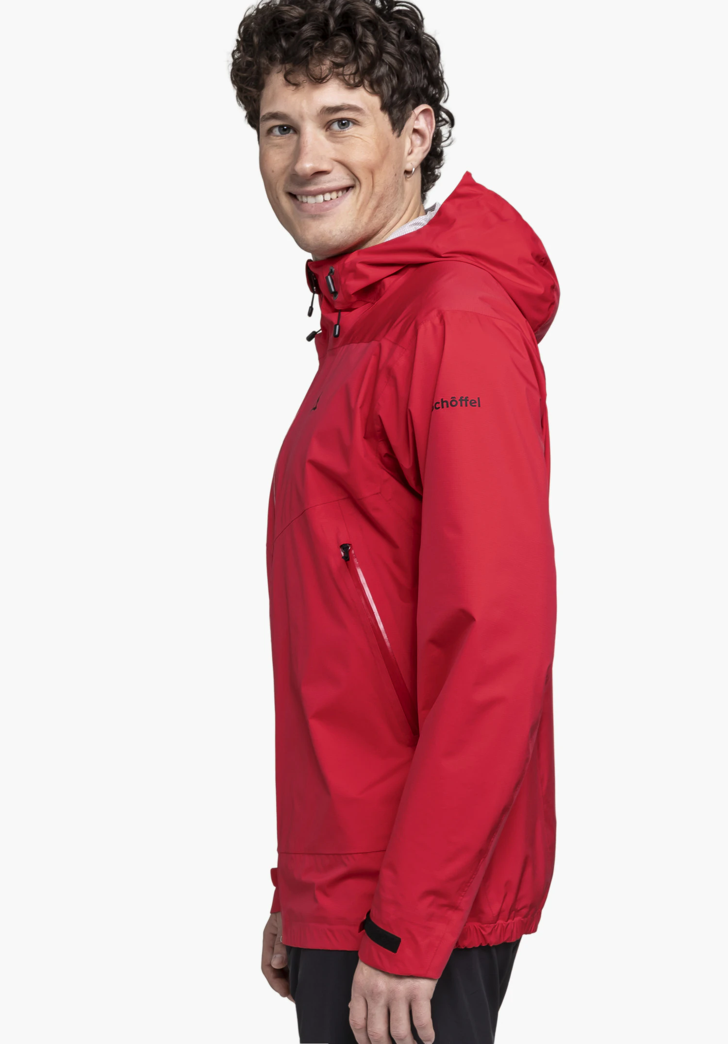 2.5L 3D Jacket Vistdal M portée par un mannequin qui se tient de profil et sourit à l'objectif. La veste rouge présente le logo Schöffel sur la manche gauche, photographiée devant un fond neutre.