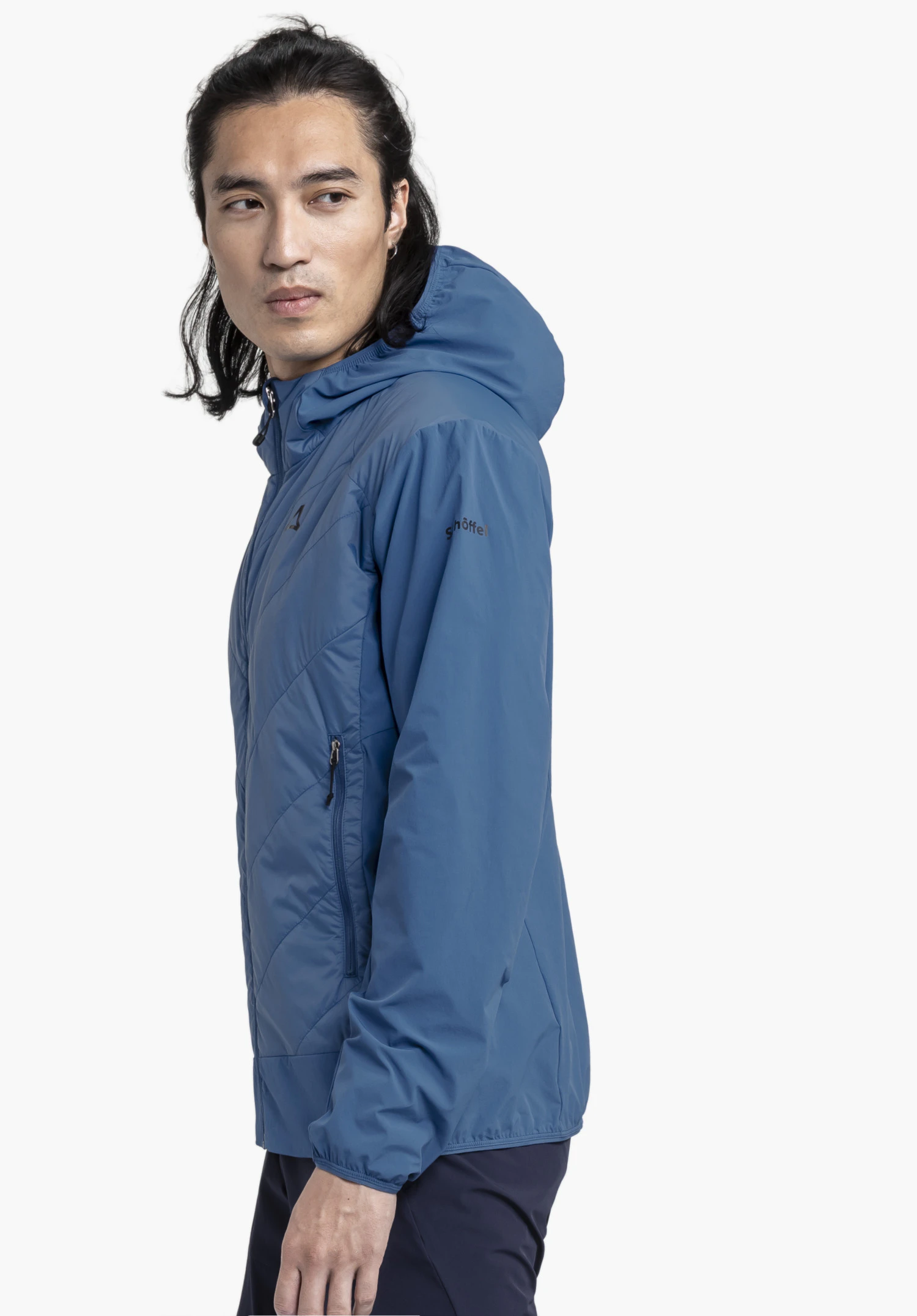 Hybrid Jk Style Blaueis MNS. Een model staat zijwaarts en toont de blauwe jas met een zichtbaar Schöffel-Logo op de mouw tegen een neutrale achtergrond.