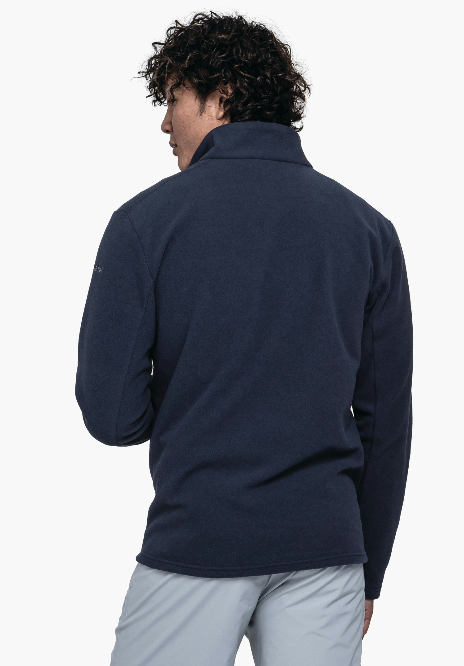 Fleece Jk Style Qutang MNS dunkelblauer Fleecepullover, von einer Person von hinten getragen, stehende Pose, hellgraue Hose, neutraler weißer Hintergrund. Text auf Ärmel: "Schöffel".