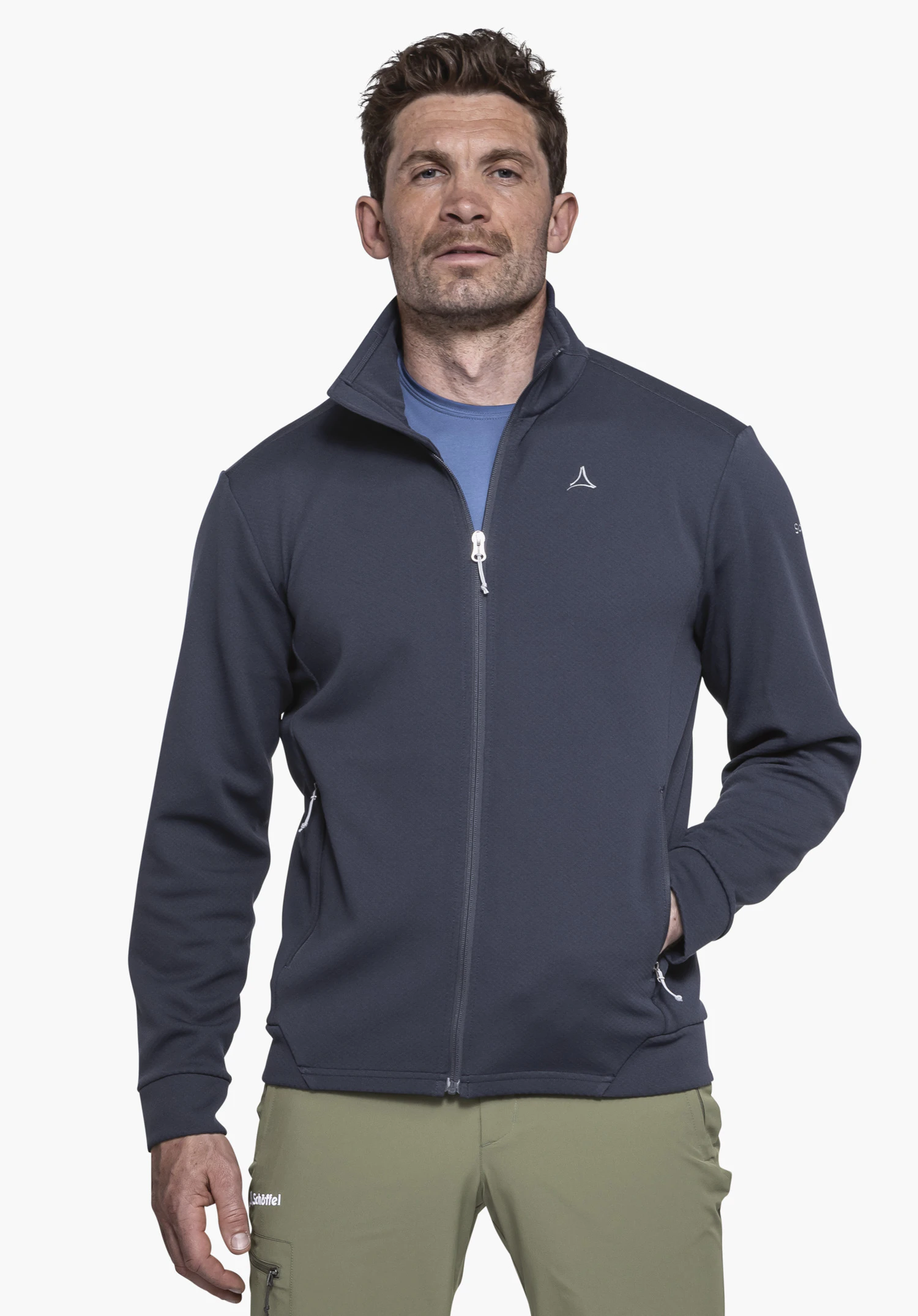 Fleece Jk Style Uriezzo MNS wird von einem Model getragen, das frontal steht und die blaue Fleecejacke mit dem sichtbaren Schöffel-Logo auf der linken Brust sowie einer Hand in der Seitentasche präsentiert, fotografiert vor einem neutralen Hintergrund.