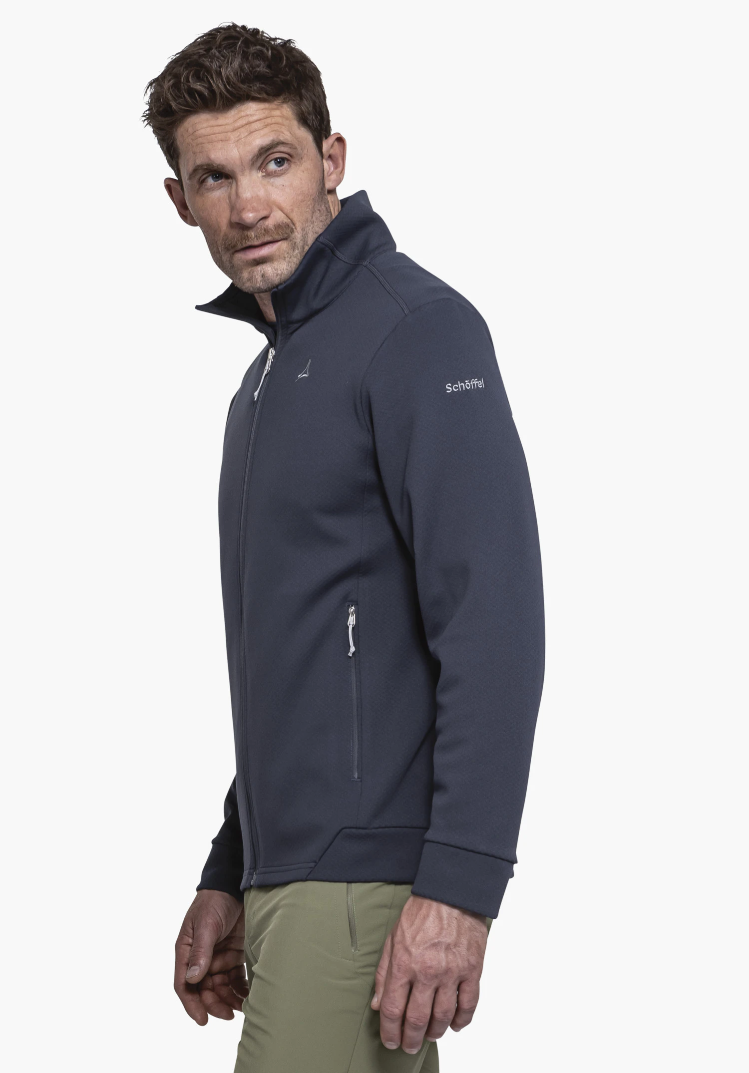 Fleece Jk Style Uriezzo MNS en bleu. Un modèle masculin est photographié de profil devant un fond neutre pour présenter la veste polaire. Le logo Schöffel est discrètement placé sur le haut du bras.